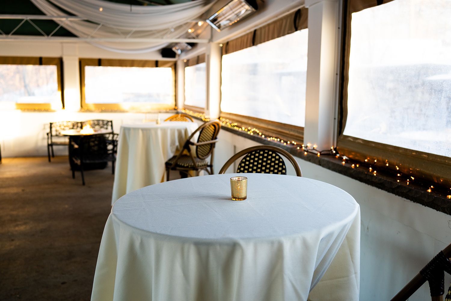A white-tablecloth wedding reception venue with round tables decorated with string lights and warm lighting.