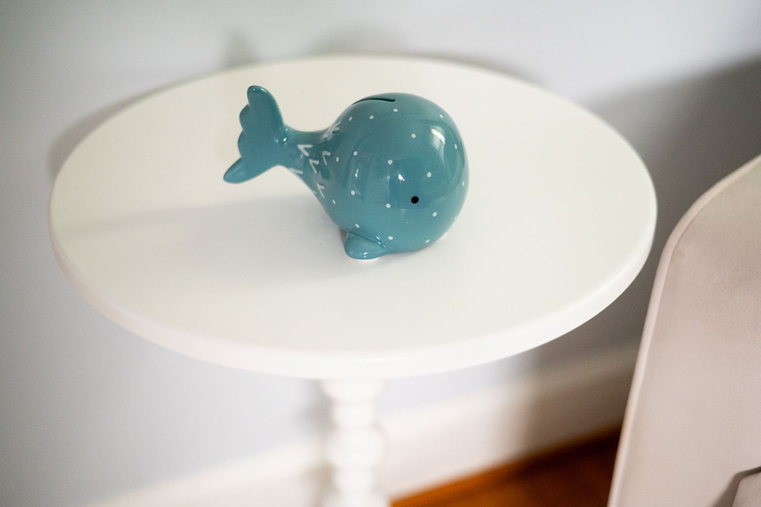 A small decorative turquoise ceramic whale sits on a white round side table.