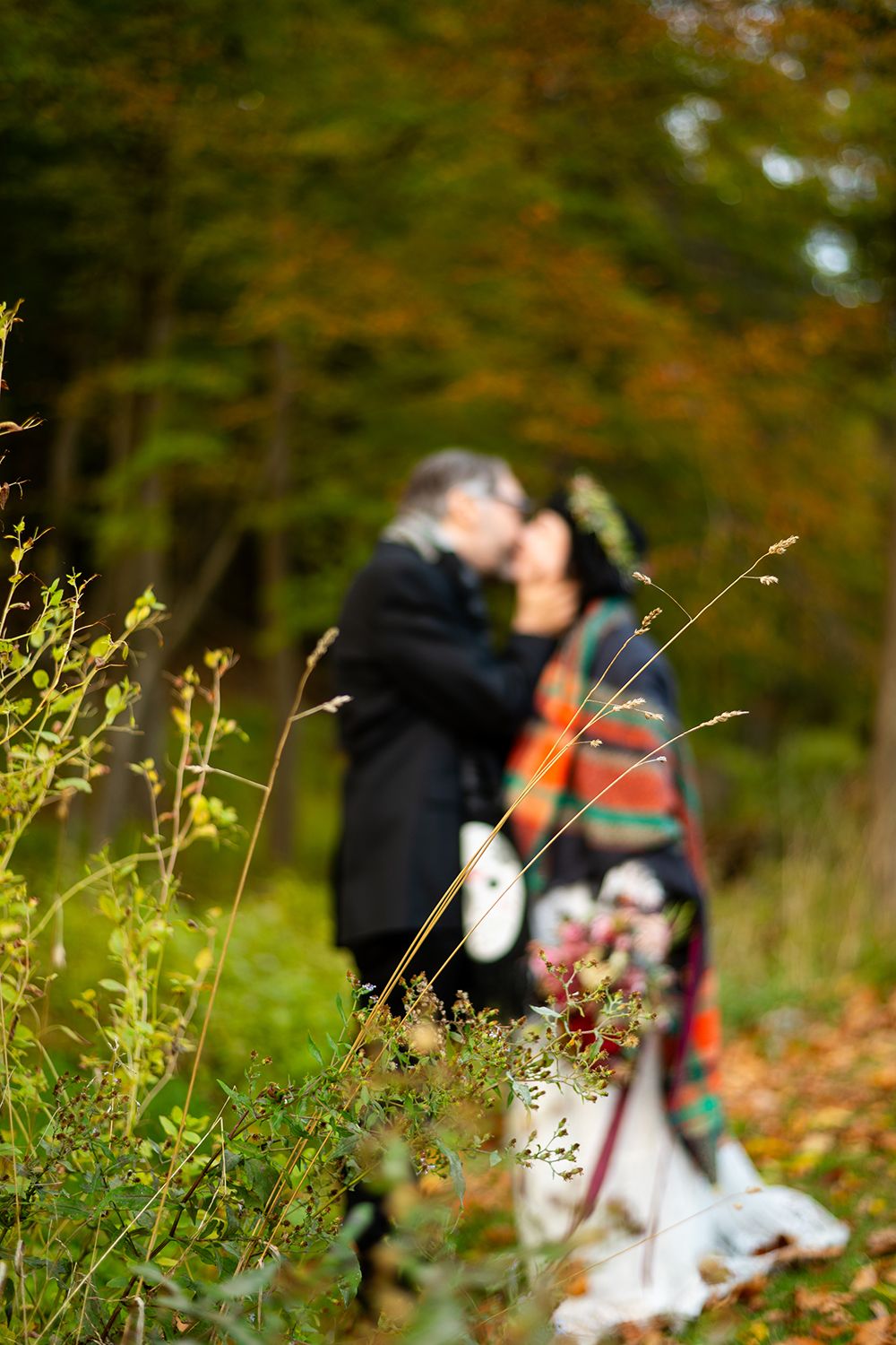 A couple shares a romantic moment in a vibrant autumn forest setting with fallen leaves and green foliage.