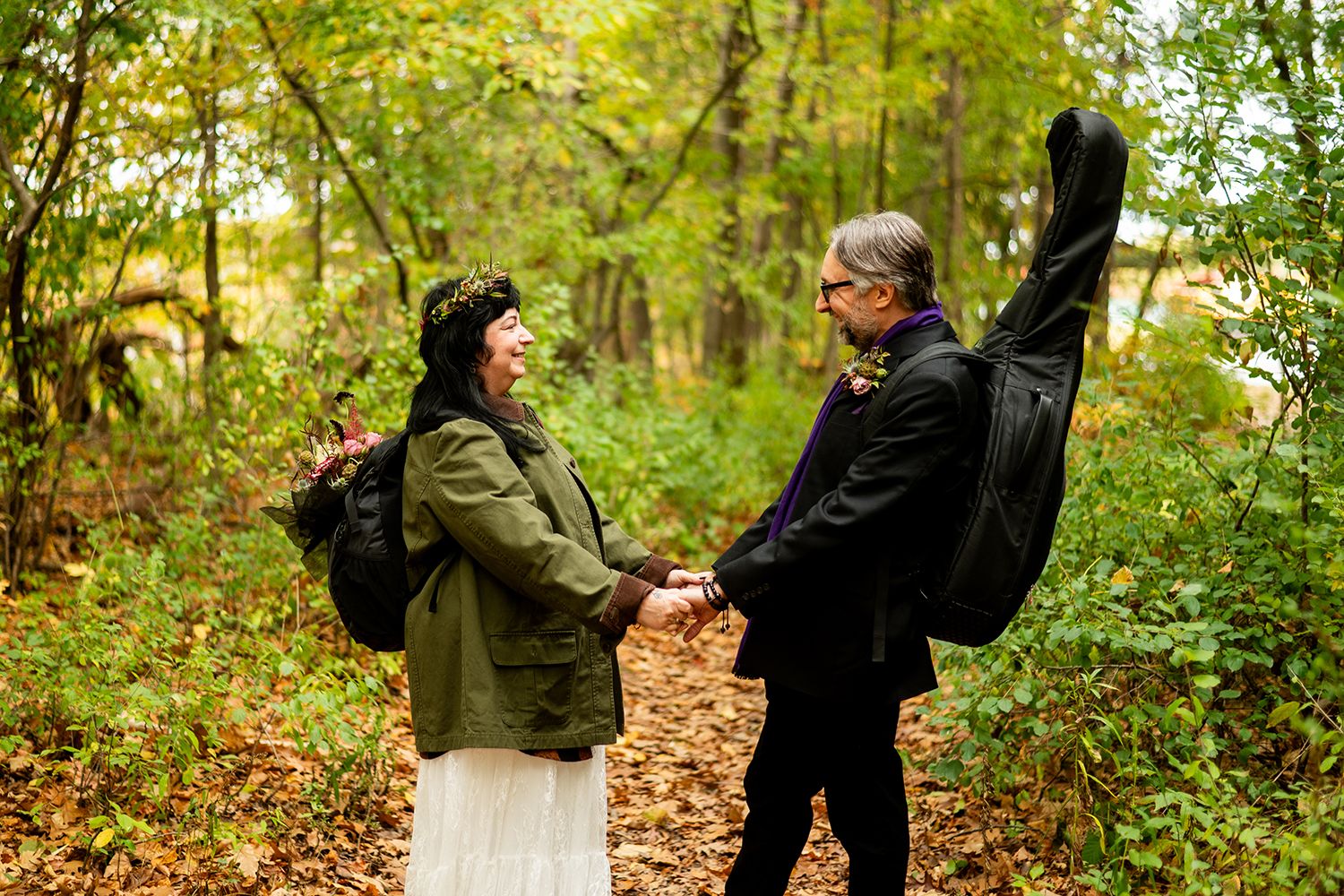 People walking through autumn forest paths with fallen leaves and green foliage in natural setting.