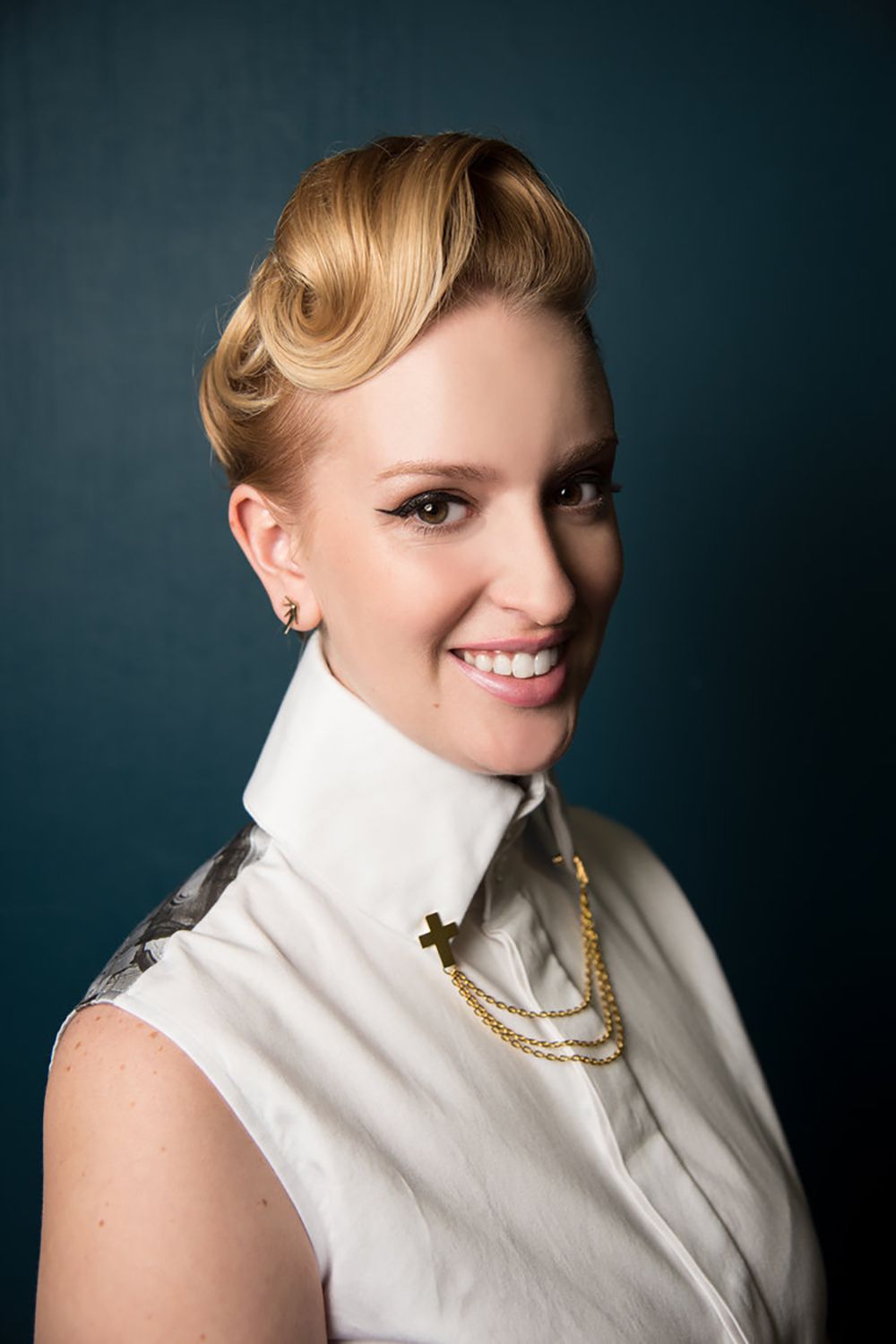 Portrait of person with elegant vintage hairstyle wearing white sleeveless top and pearl necklace against dark background.