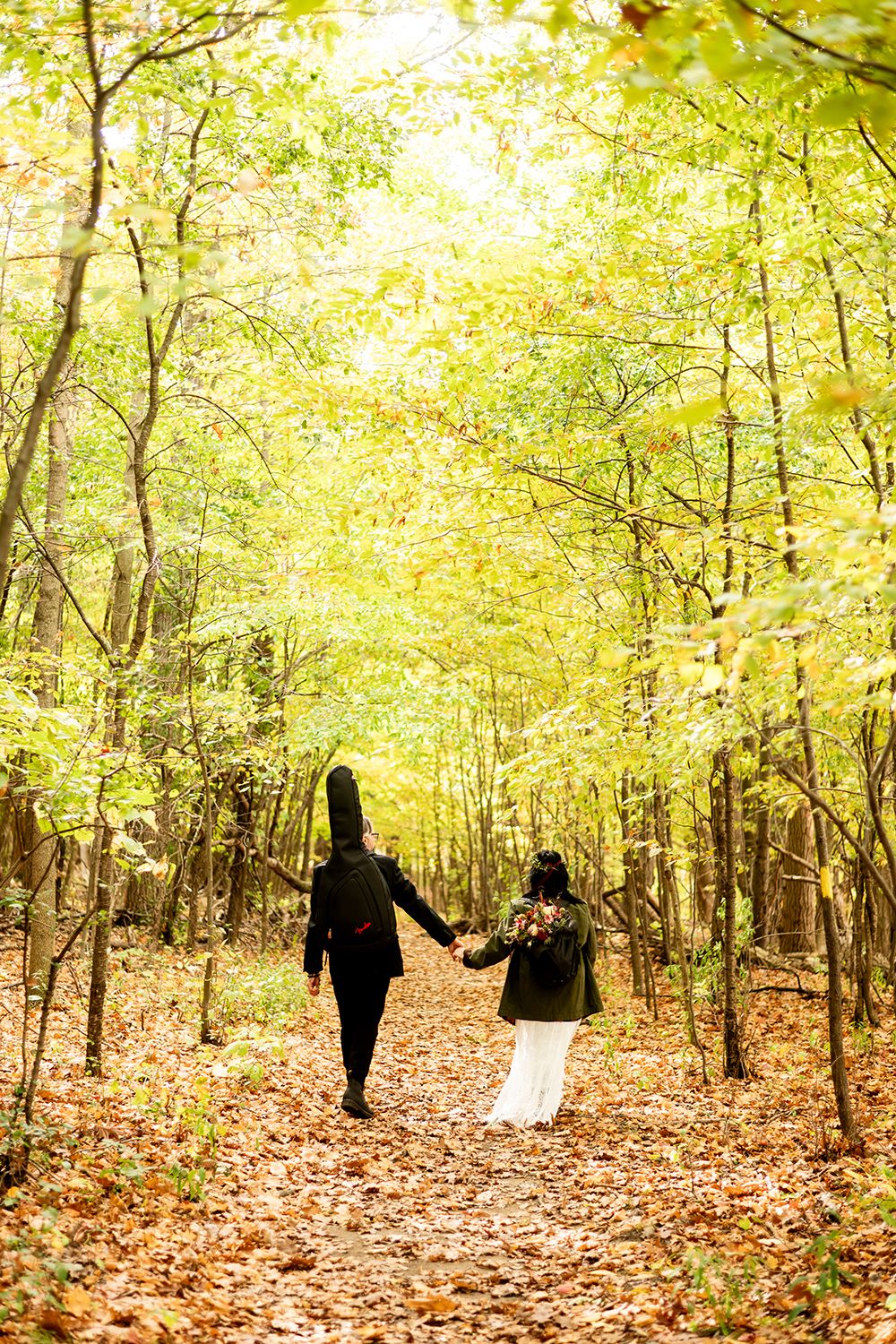 Silhouettes of people walking through autumn forest with golden leaves scattered on ground during fall photoshoot.