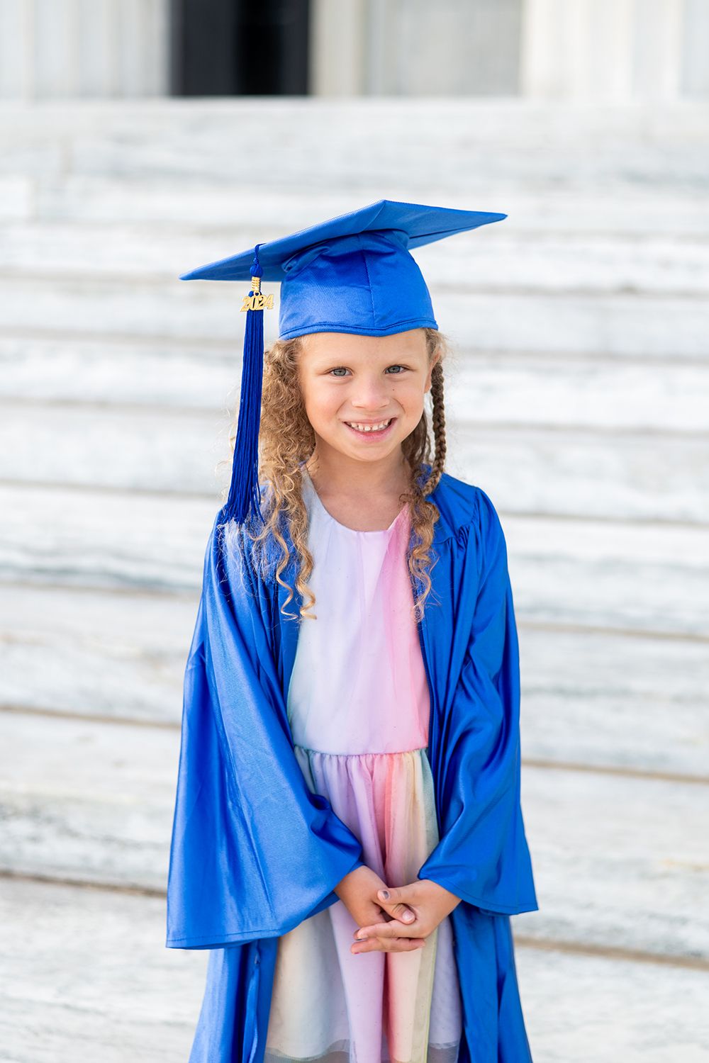 Graduate in bright blue cap and gown stands on white steps during graduation ceremony.