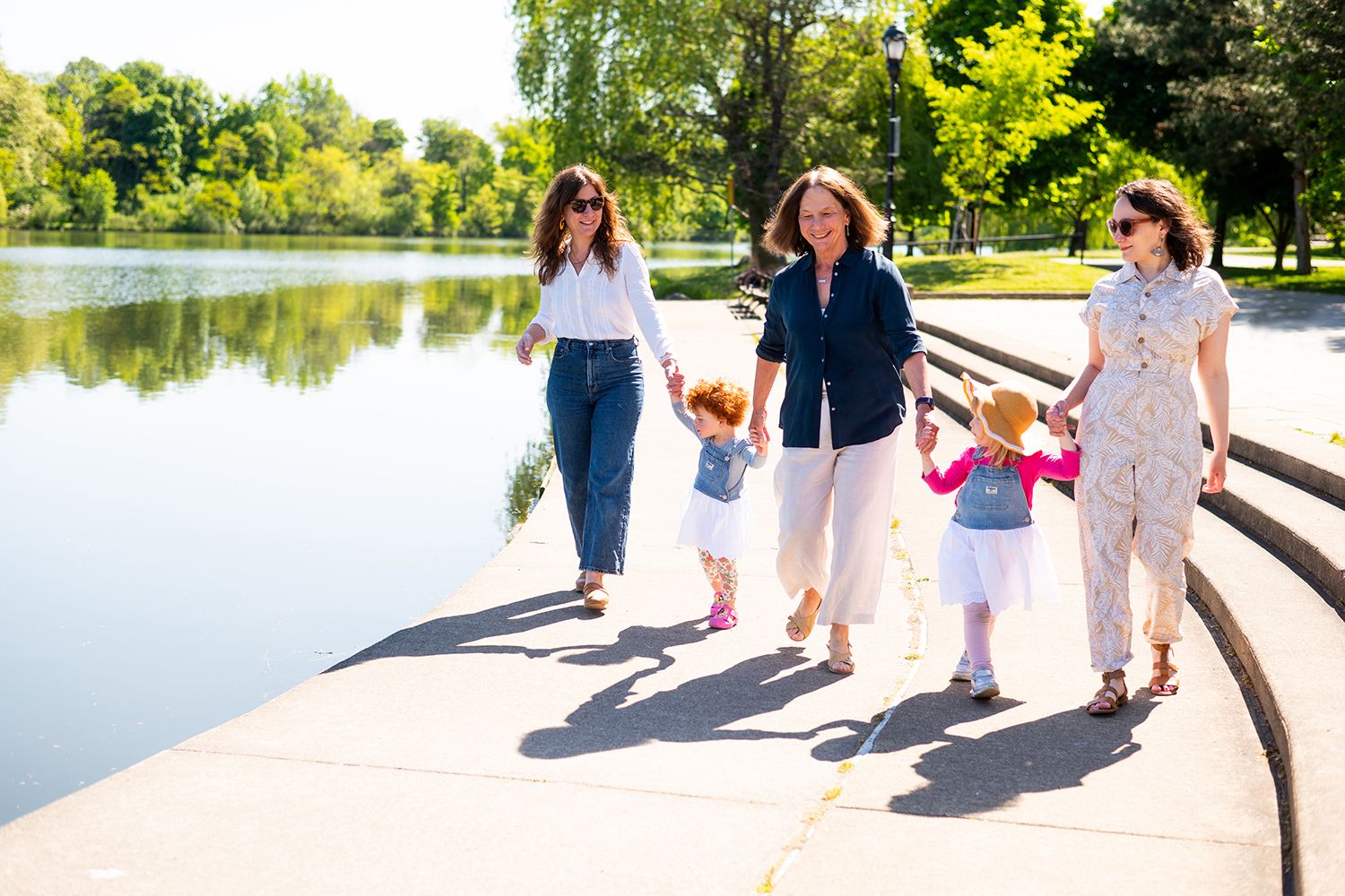 Group strolling together on scenic waterfront pathway with lake and greenery in background.