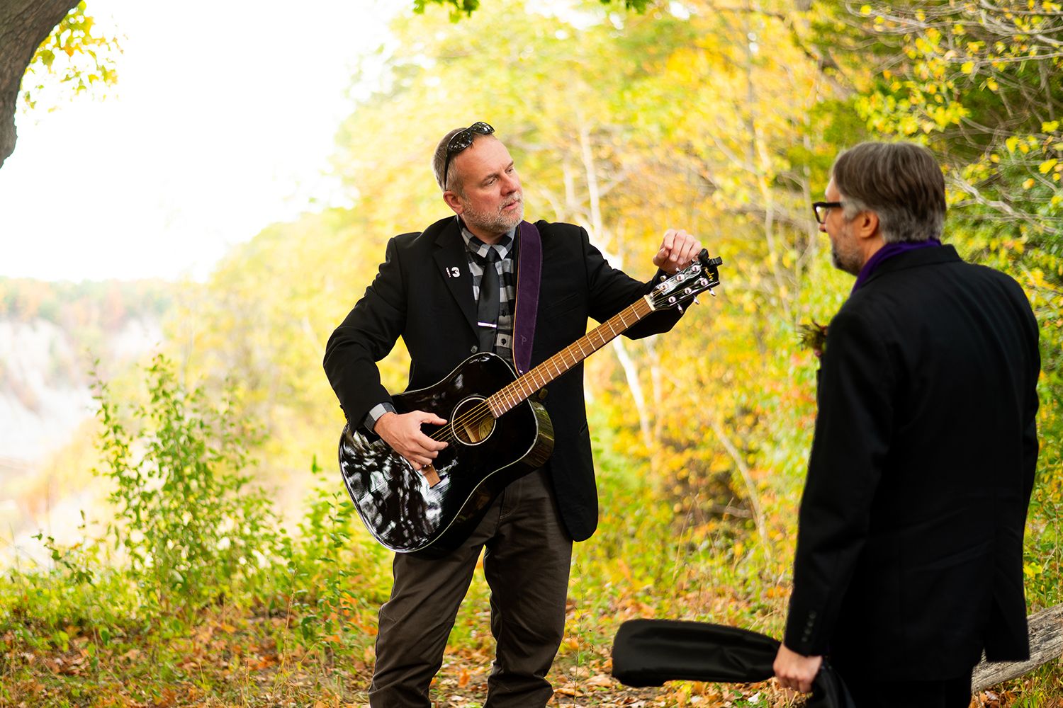 Musicians perform with acoustic guitars outdoors in autumn foliage at a scenic outdoor location.