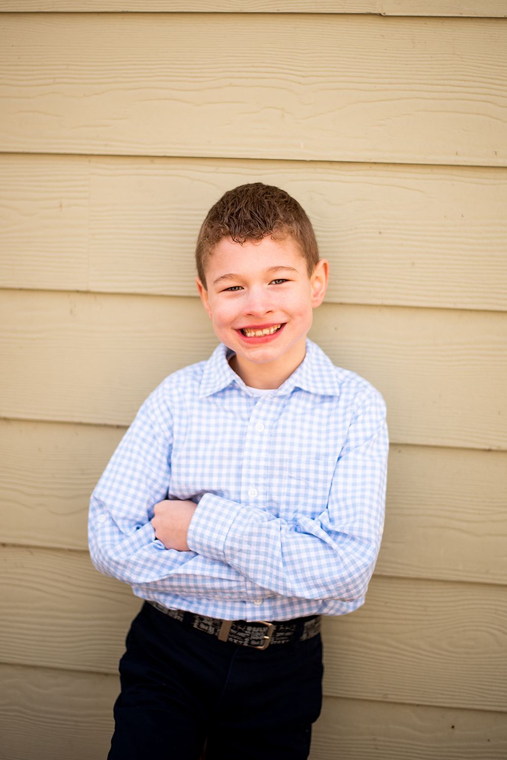 Portrait of youth in blue gingham shirt smiling warmly against beige siding.