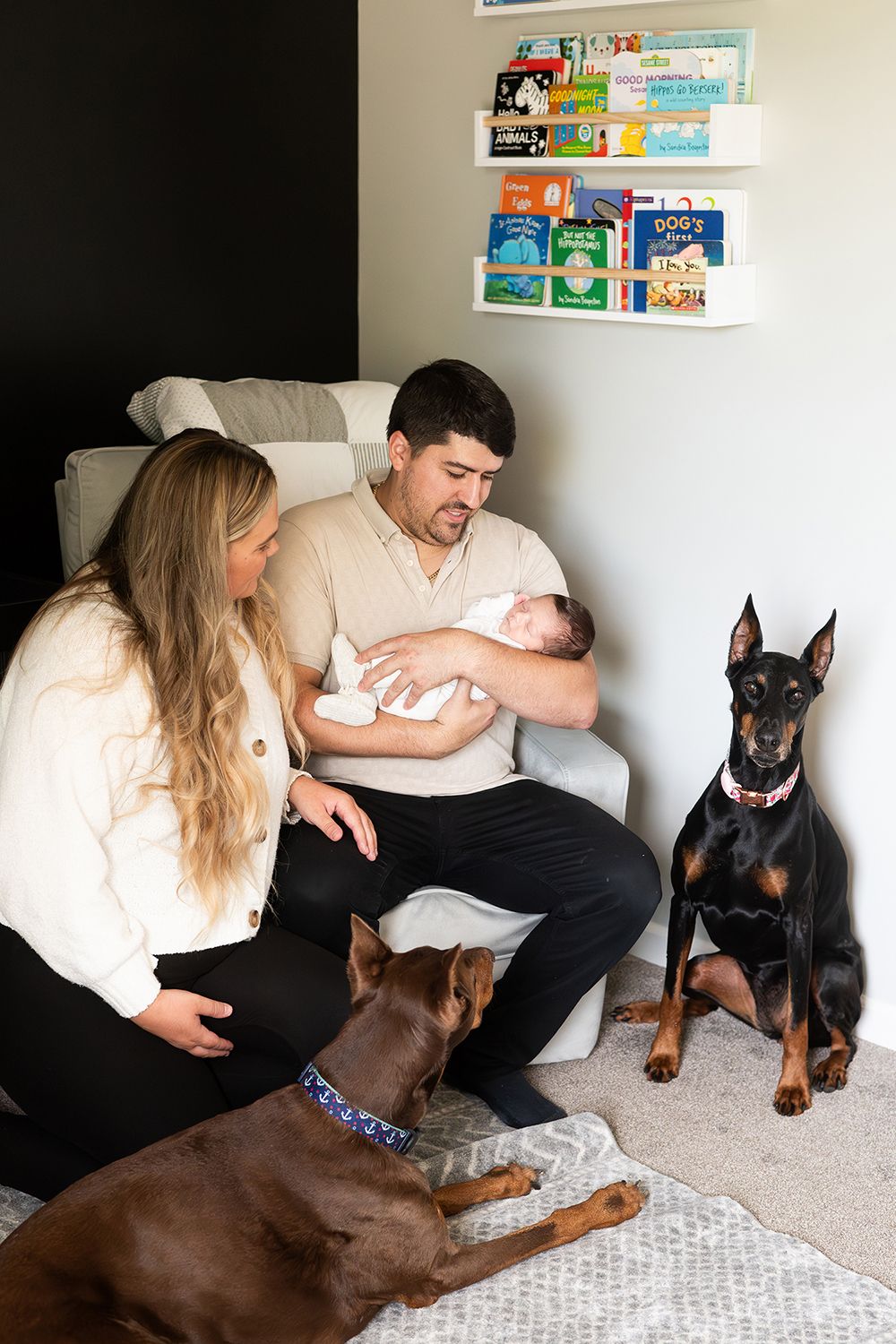 Young couple sitting in a nursery with their newborn baby and two attentive dogs relaxing on the floor.
