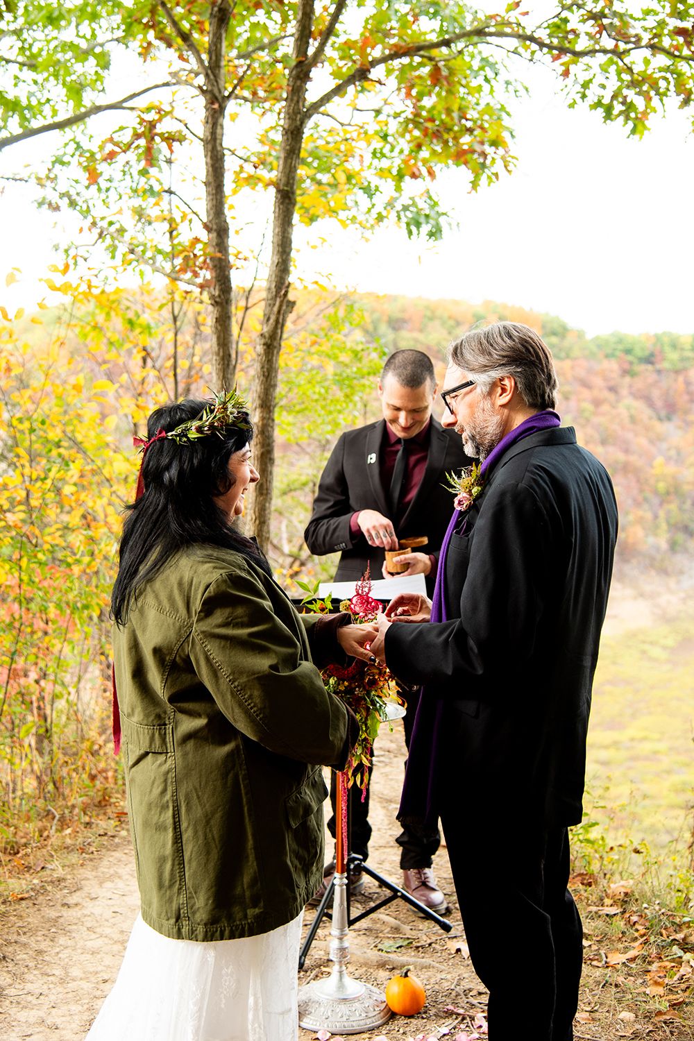 A couple exchanges vows during an intimate outdoor autumn ceremony on a wooded path.