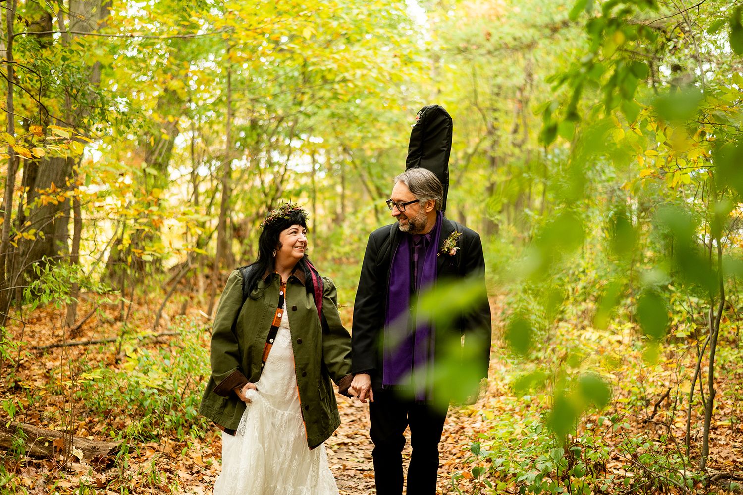 A couple walks through a vibrant autumn forest setting with golden leaves and natural sunlight filtering through trees.