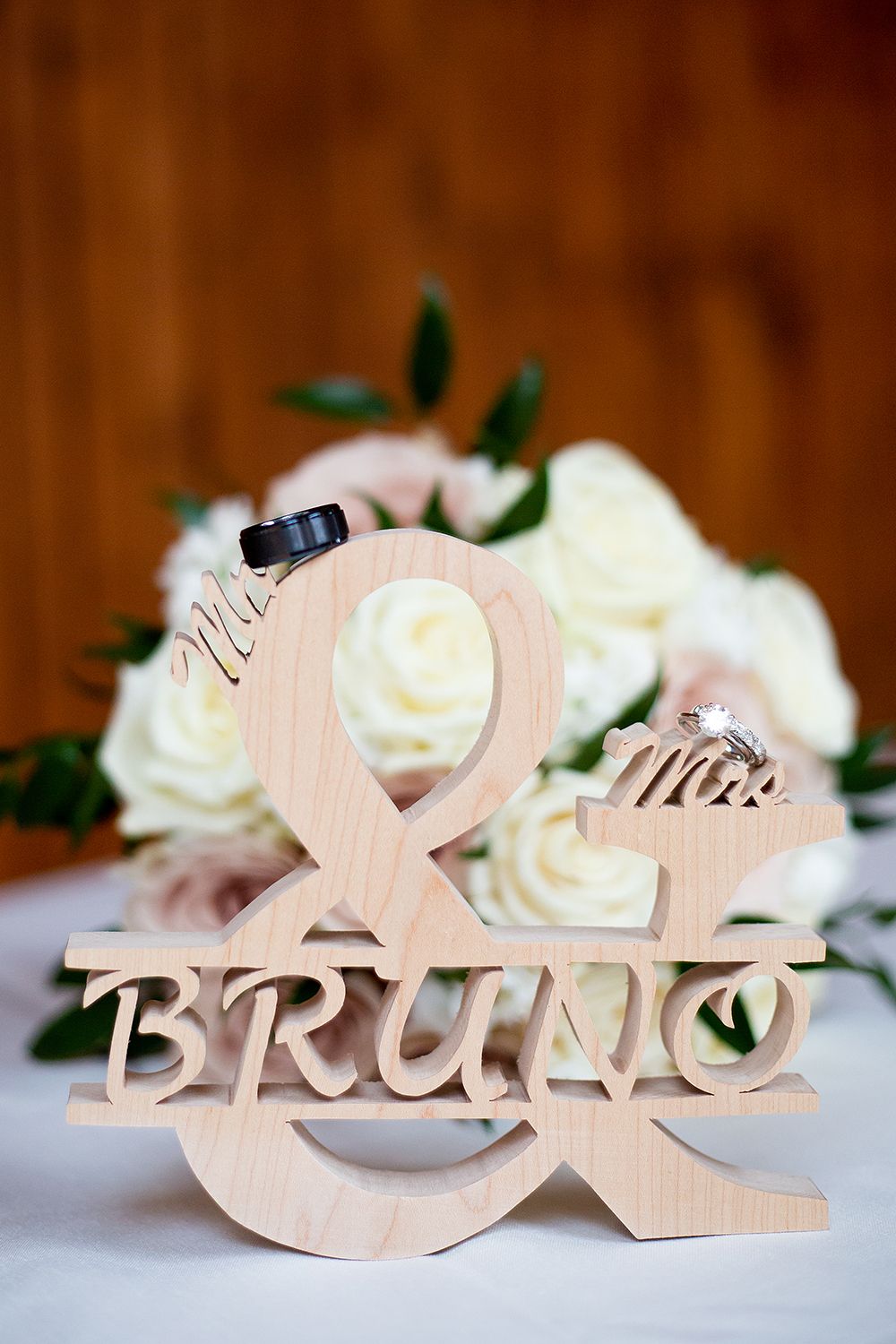 Wooden wedding name signs spelling 'Mr & Mrs Bruno' arranged with white roses against rustic backdrop.