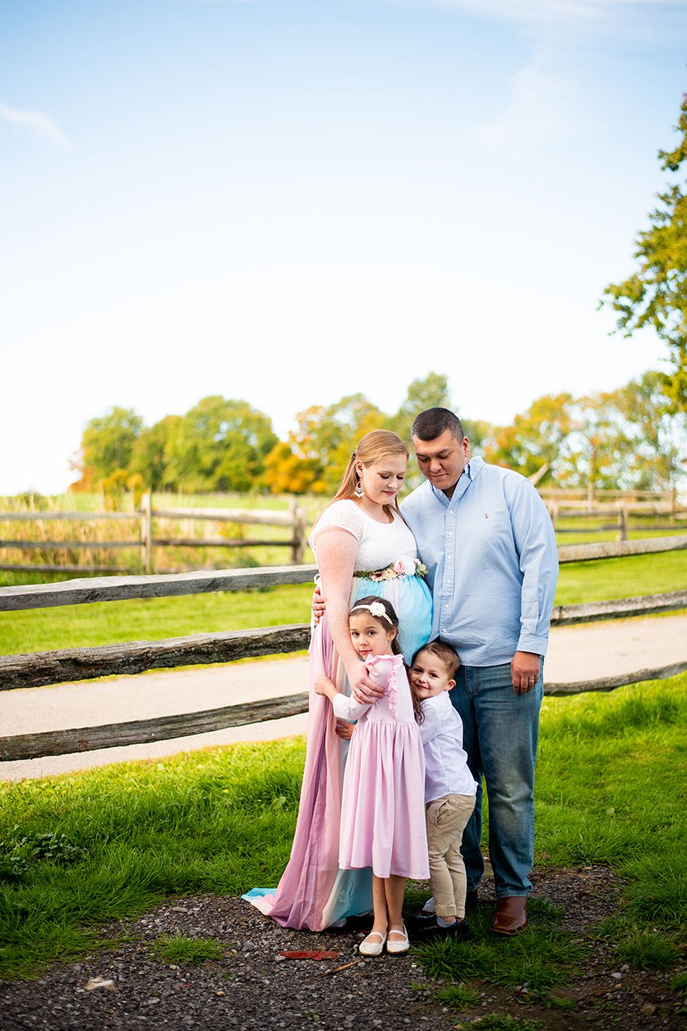 Family shares tender moments together outdoors on a sunny day in front of wooden split-rail fence.