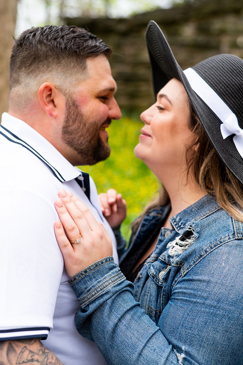 A close romantic moment between a couple outdoors, with one wearing a denim jacket and black hat against a blurred natural backdrop.
