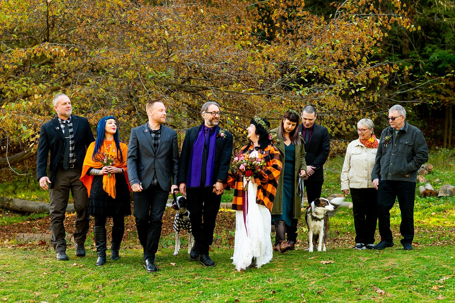 Wedding party poses together on autumn lawn with colorful fall foliage in background.