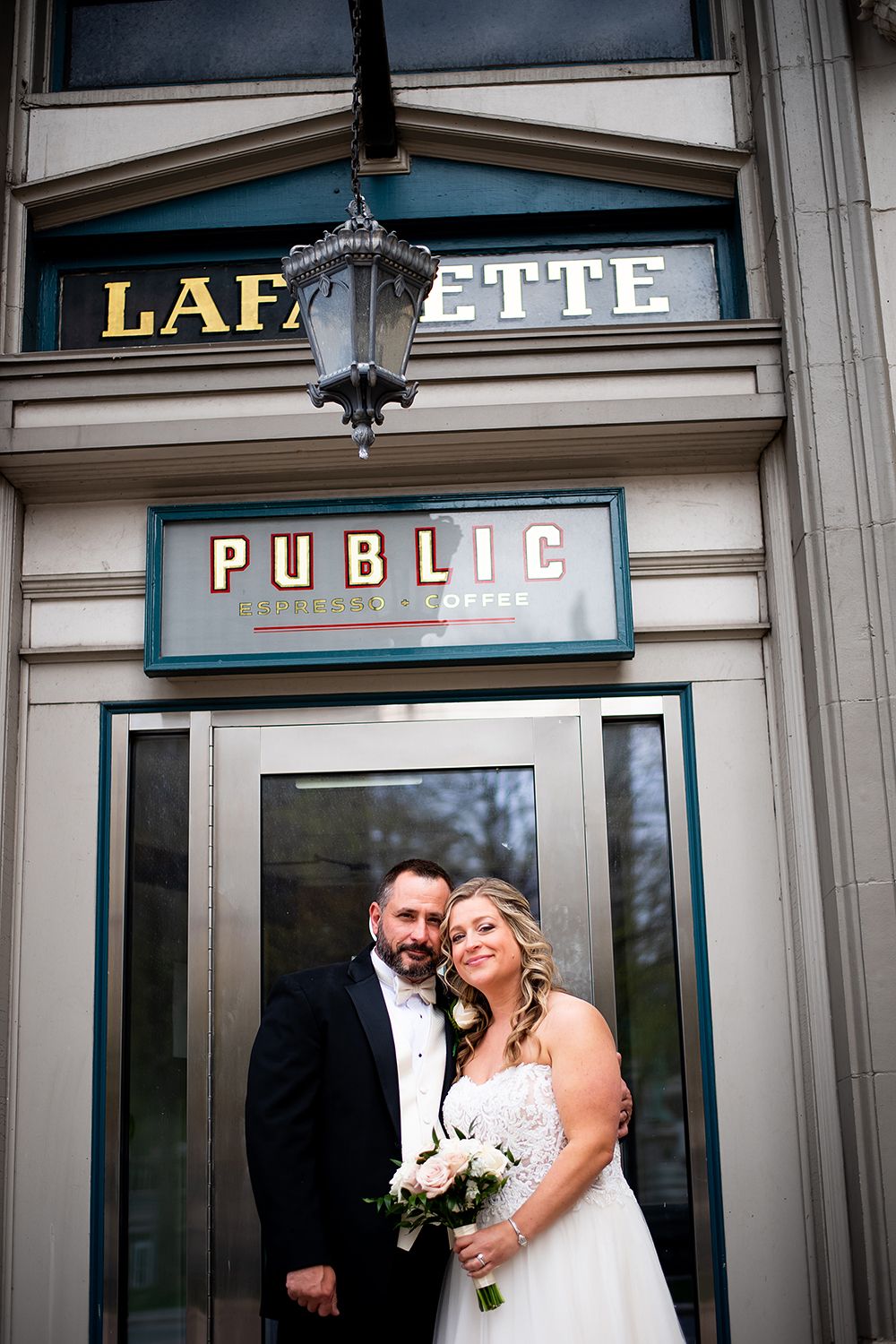 A wedding couple poses for a portrait in front of the historic Lafayette Public entrance.