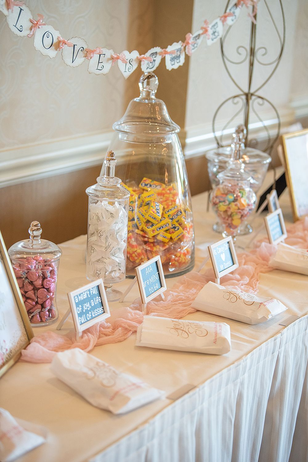 A romantic candy buffet table with glass jars of colorful sweets under a 'LOVE' banner at a wedding reception.