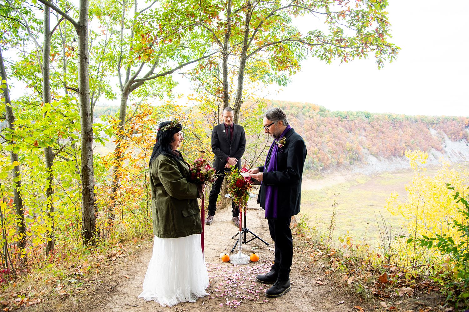 People gather in an autumn forest setting for what appears to be an intimate ceremony among golden-leaved trees.