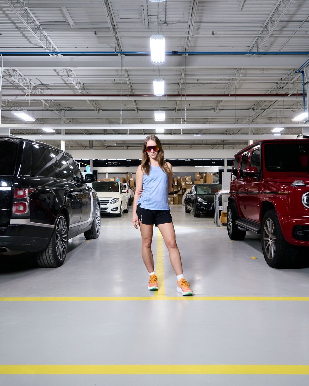 A woman strolls through a parking garage, with various cars parked in neat rows around him.