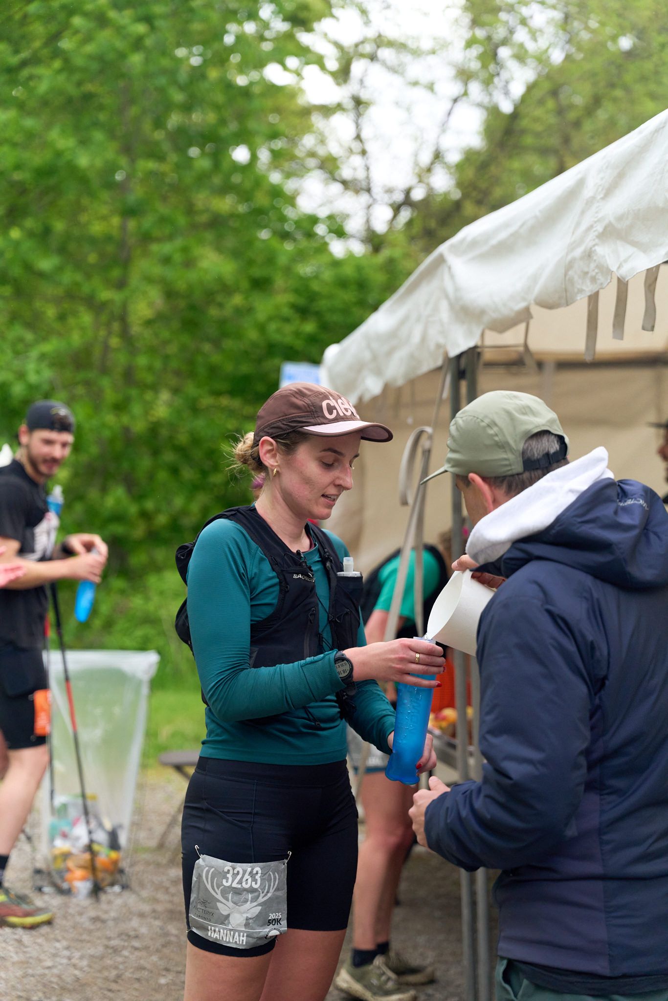A man and woman engaged in conversation at a race, surrounded by spectators and colorful banners in the background.