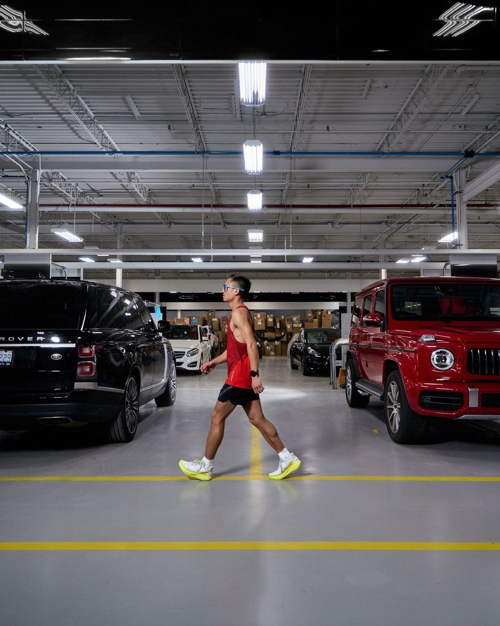 A man walks through a dimly lit parking garage surrounded by parked cars on either side.