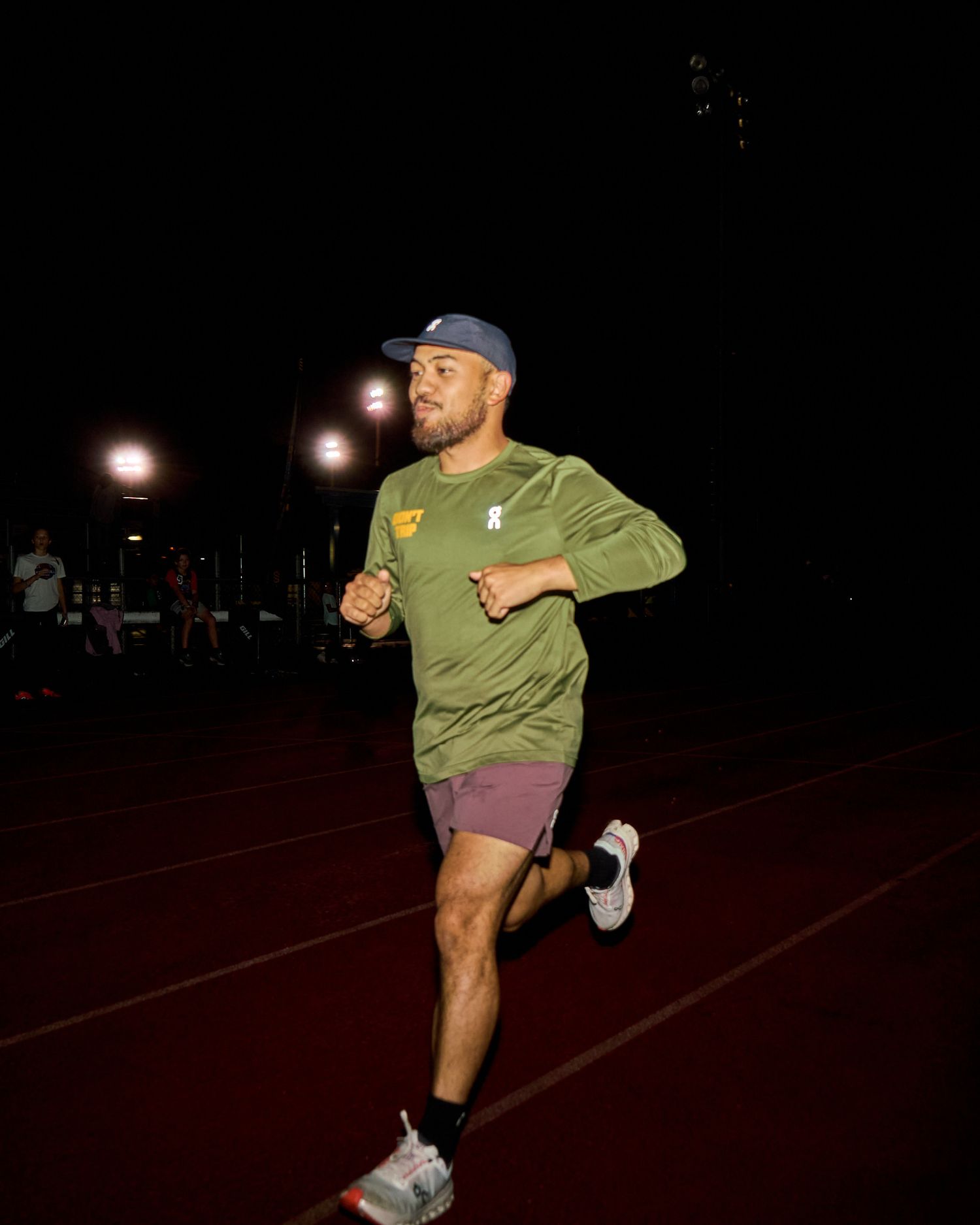 A man sprinting on a track under the night sky, illuminated by stadium lights.