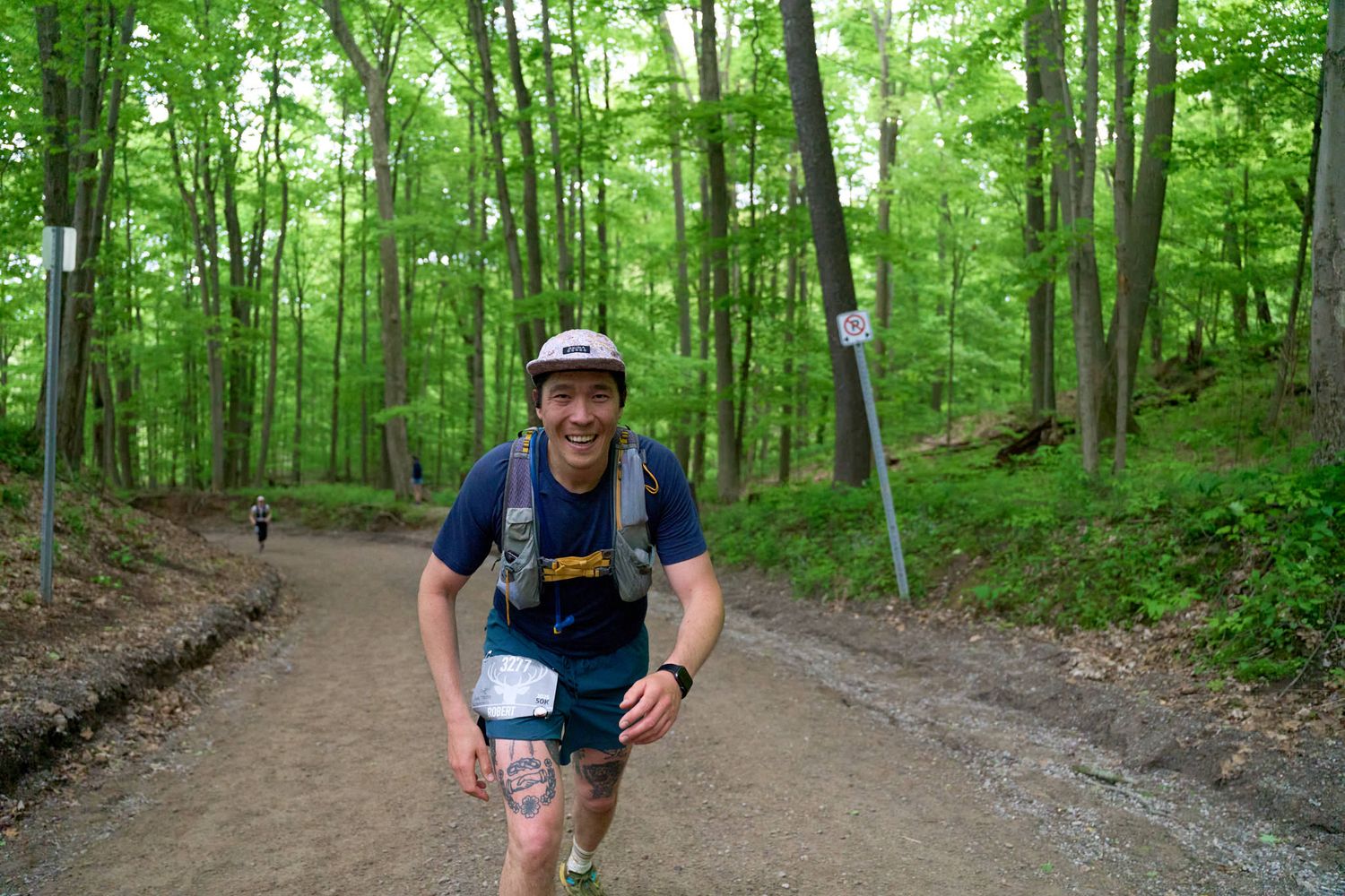 A man with sprints through a wooded area, with greenery and sunlight filtering through the trees.