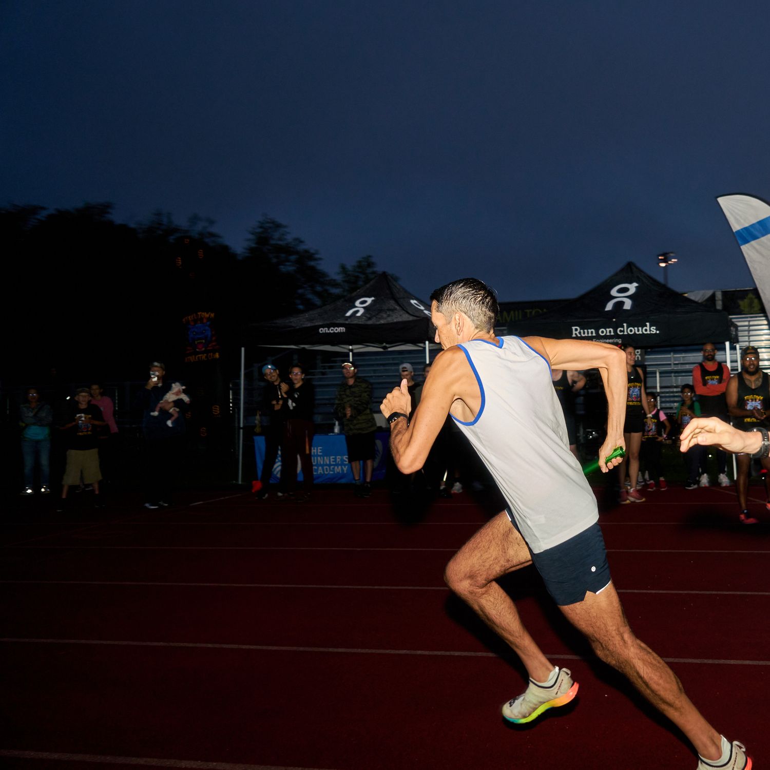 A man sprinting on a track under the night sky, illuminated by stadium lights.