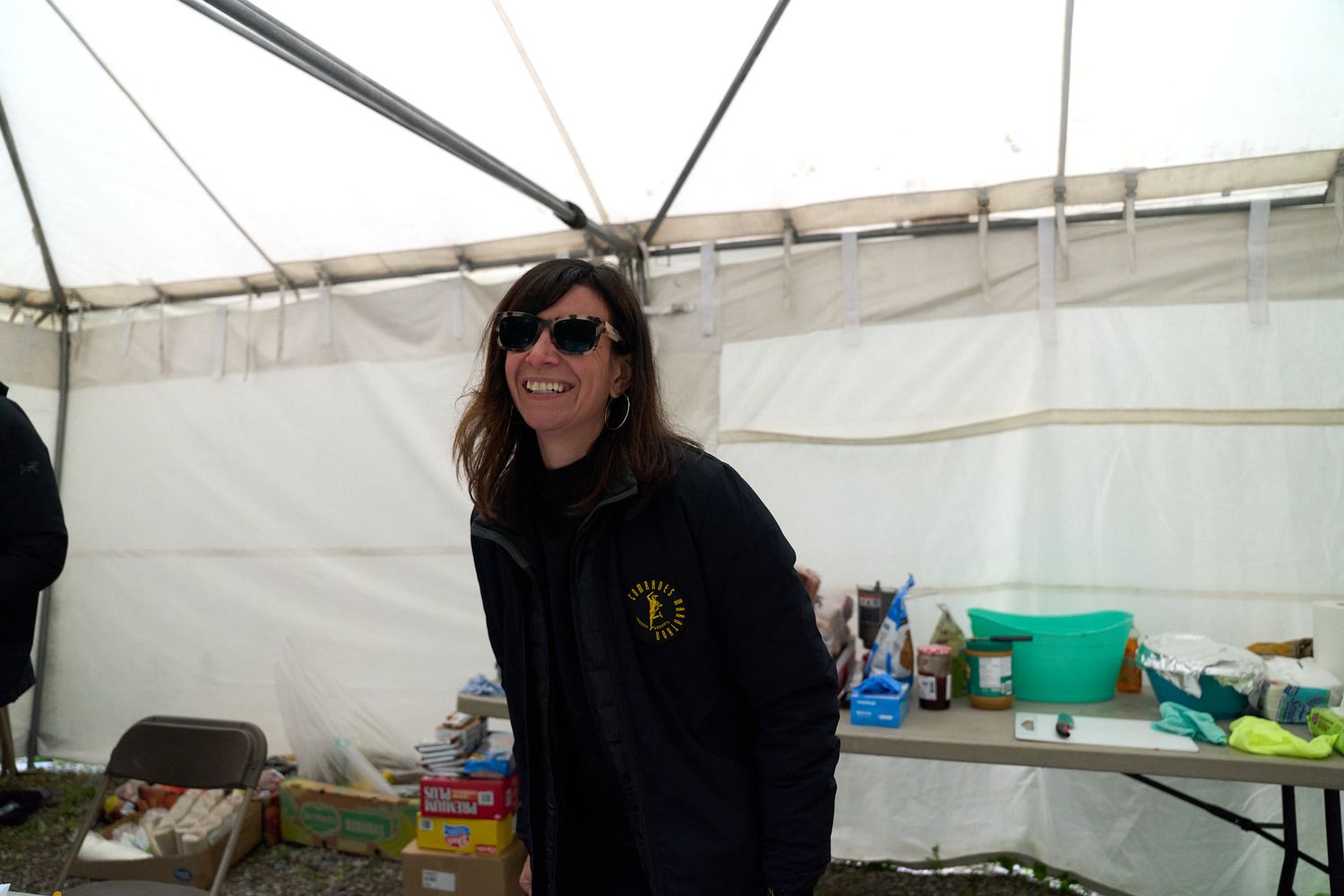 A woman wearing sunglasses stands beside a table filled with various dishes and food items.