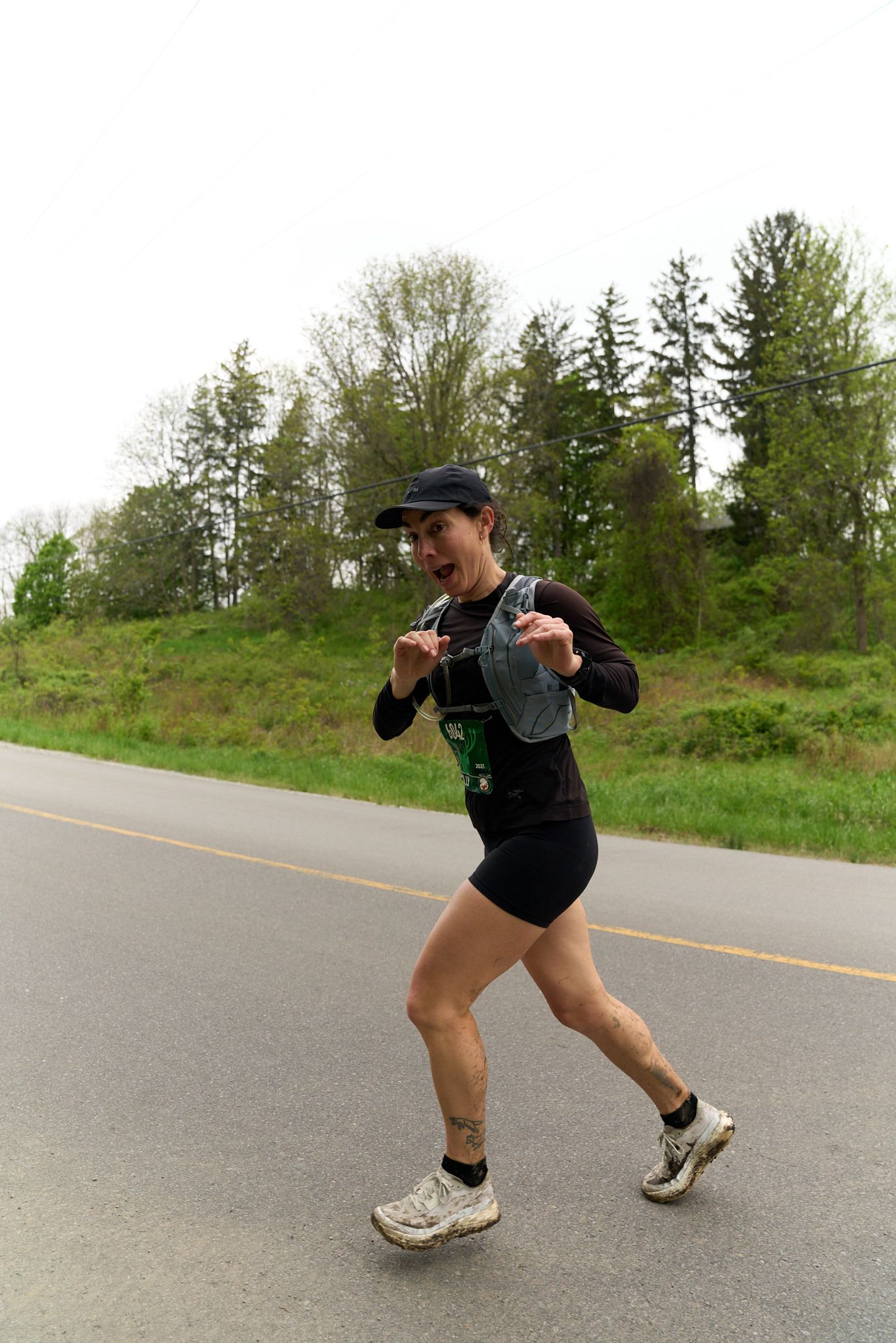 A woman with a backpack jogs on a road, surrounded by greenery and a clear blue sky.