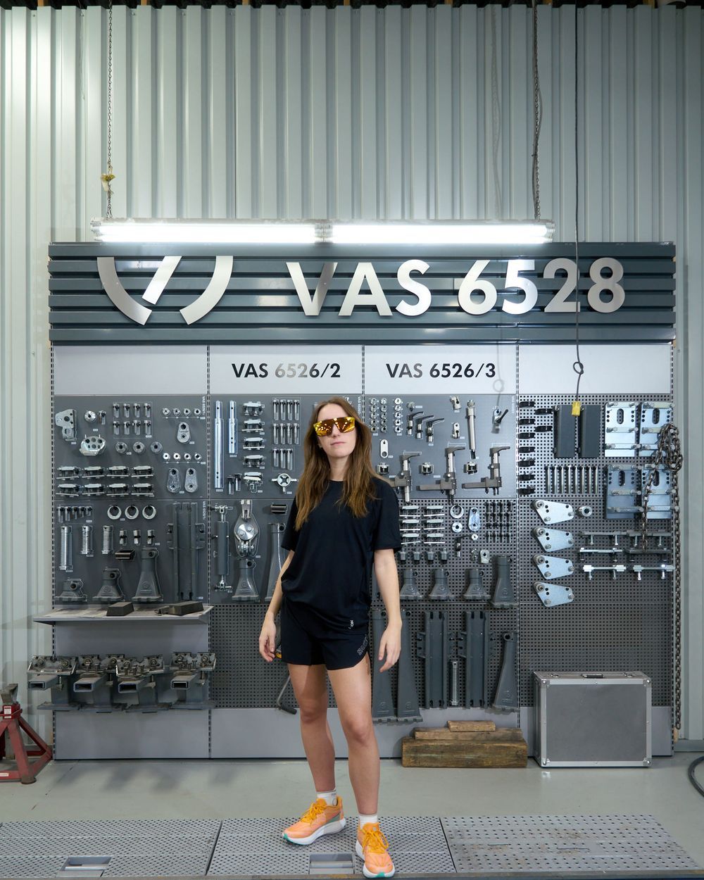 A woman strolls through a parking garage, with various cars parked in neat rows around him.
