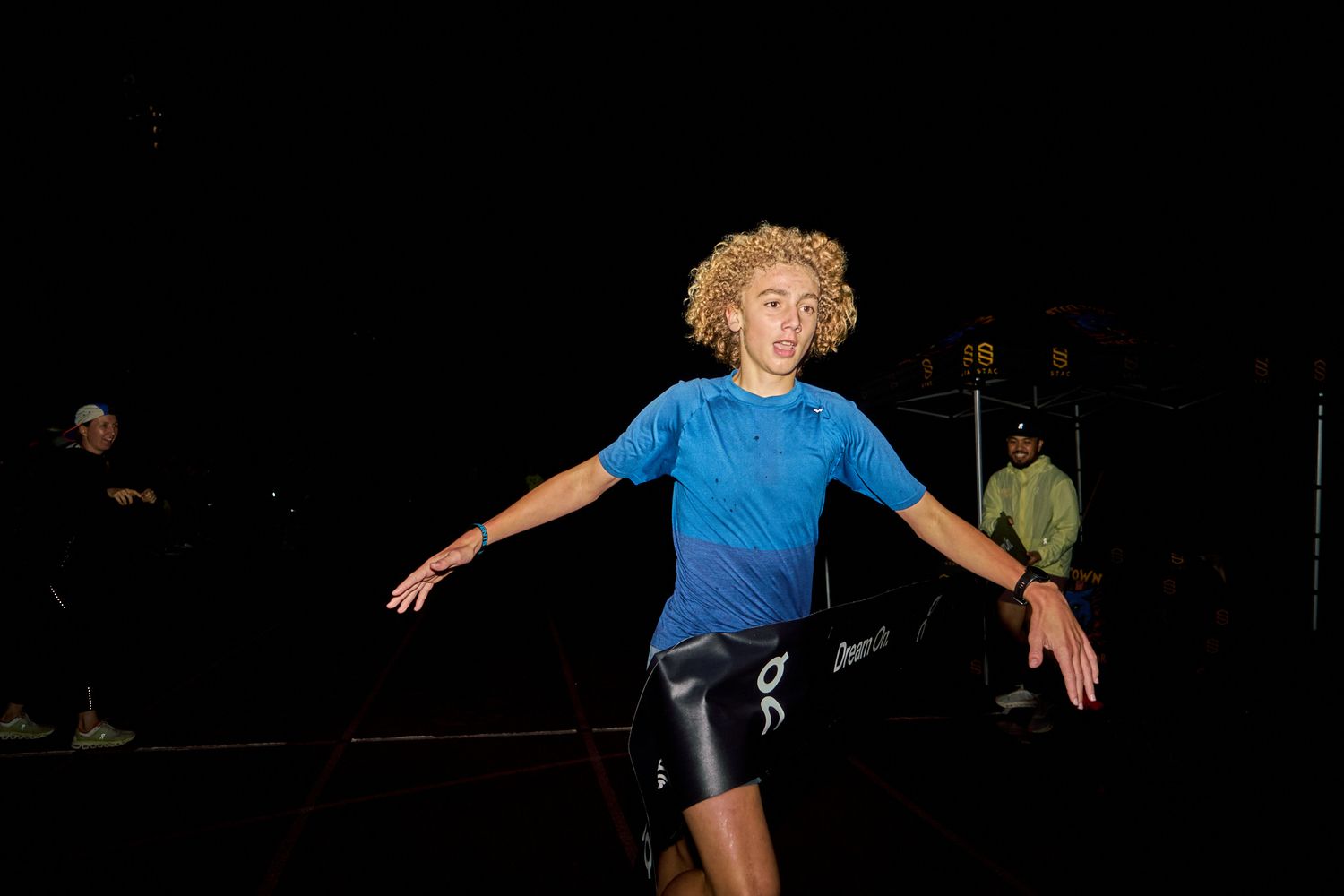 A man in motion on a track at night, surrounded by darkness and bright stadium lights.