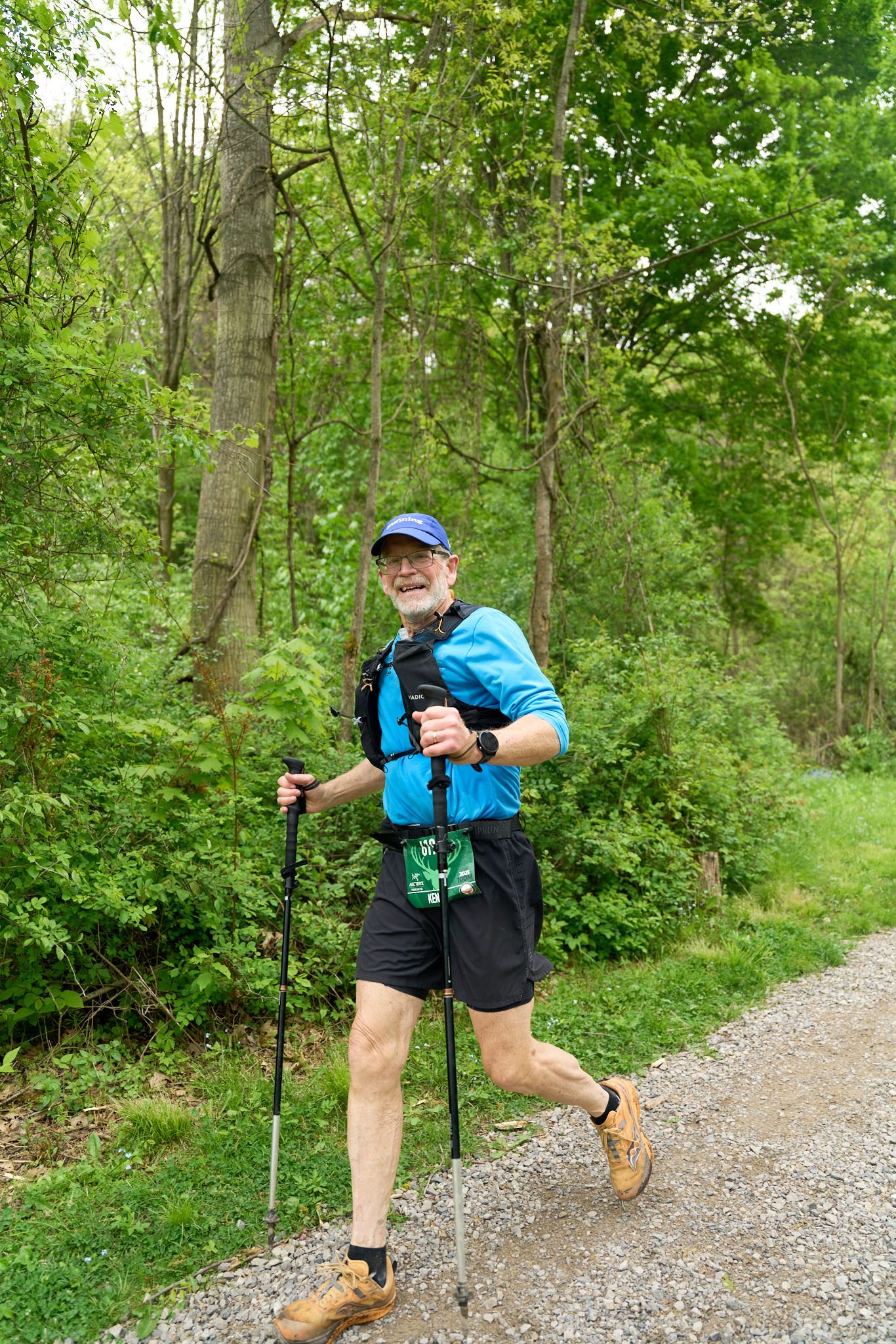 A man in a blue tank top and sunglasses jogs along a path.