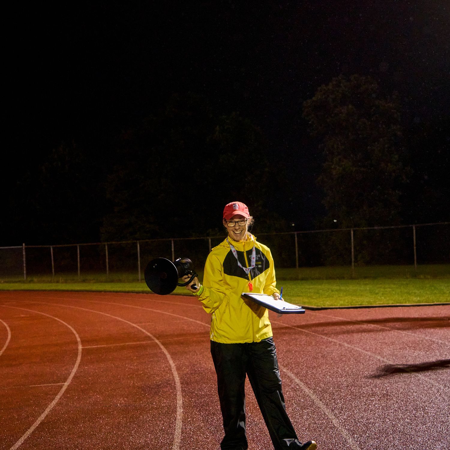 A woman in motion, running on a track at night, surrounded by darkness and bright lights.