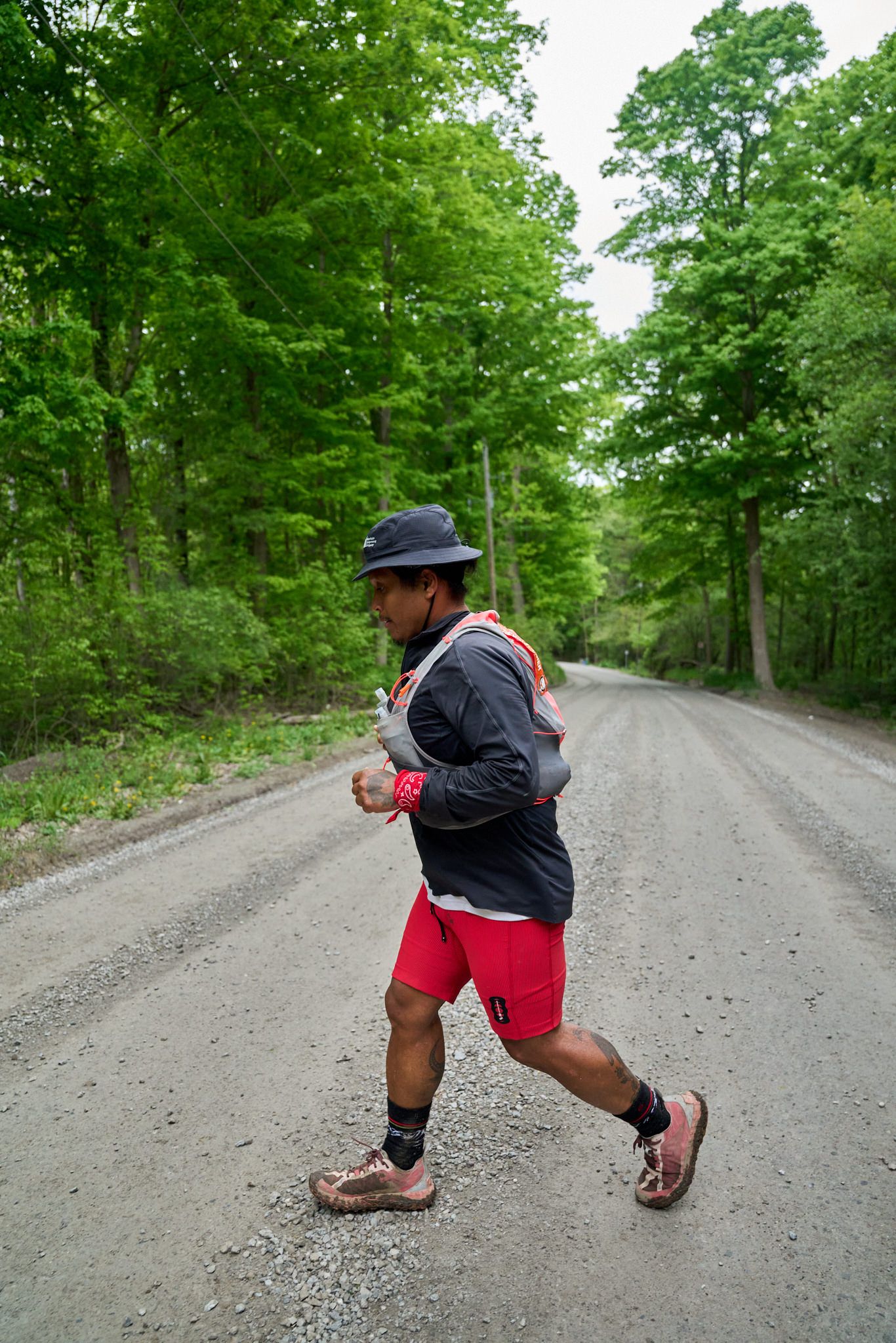 A man wearing a hat and red shorts runs along a road, showcasing an active outdoor lifestyle.