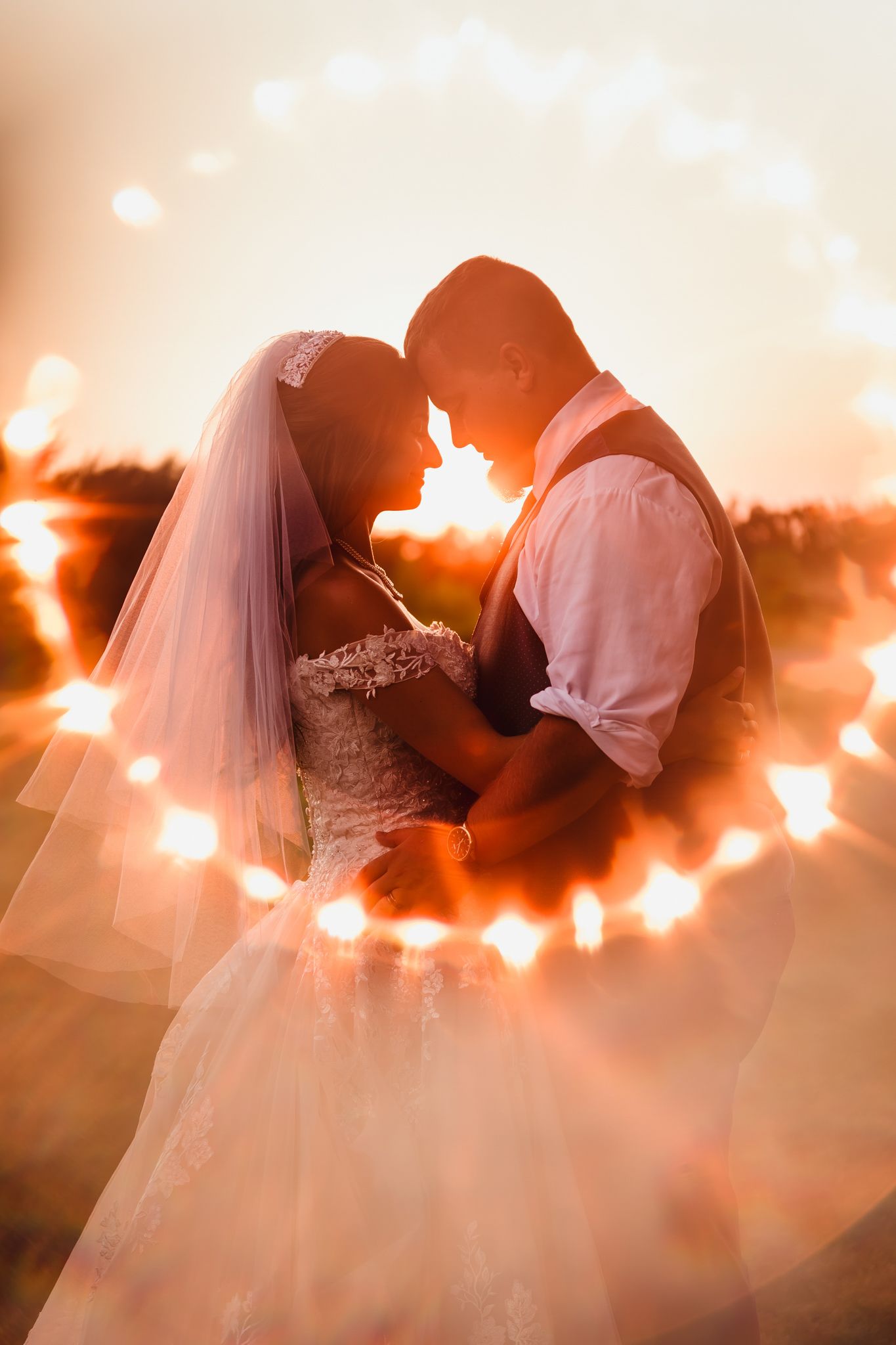 A couple in wedding attire sharing a romantic silhouetted moment at sunset with glowing lights creating a magical atmosphere.