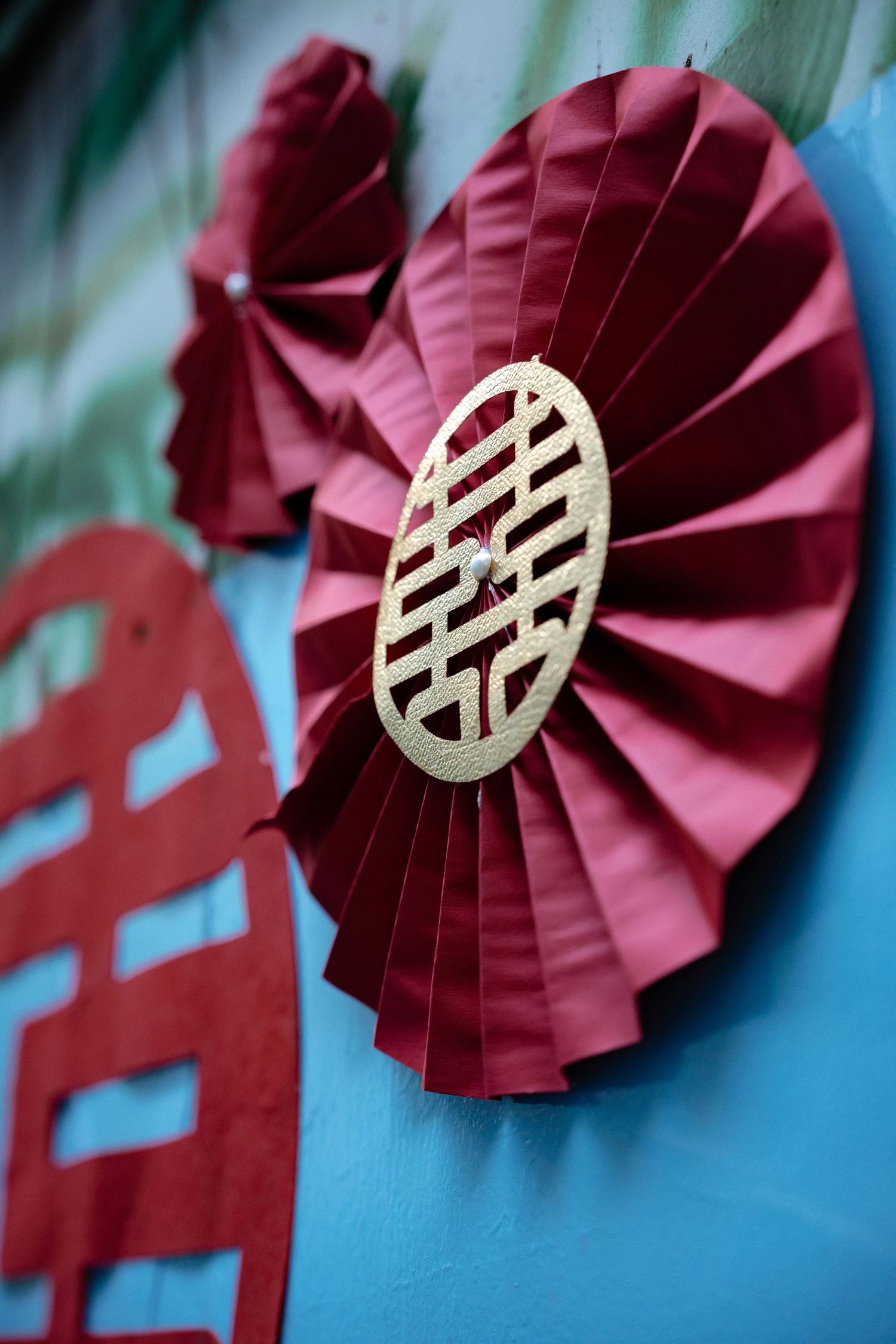 Red paper fan decoration with Chinese double happiness symbol displayed against blue background for traditional wedding decor.