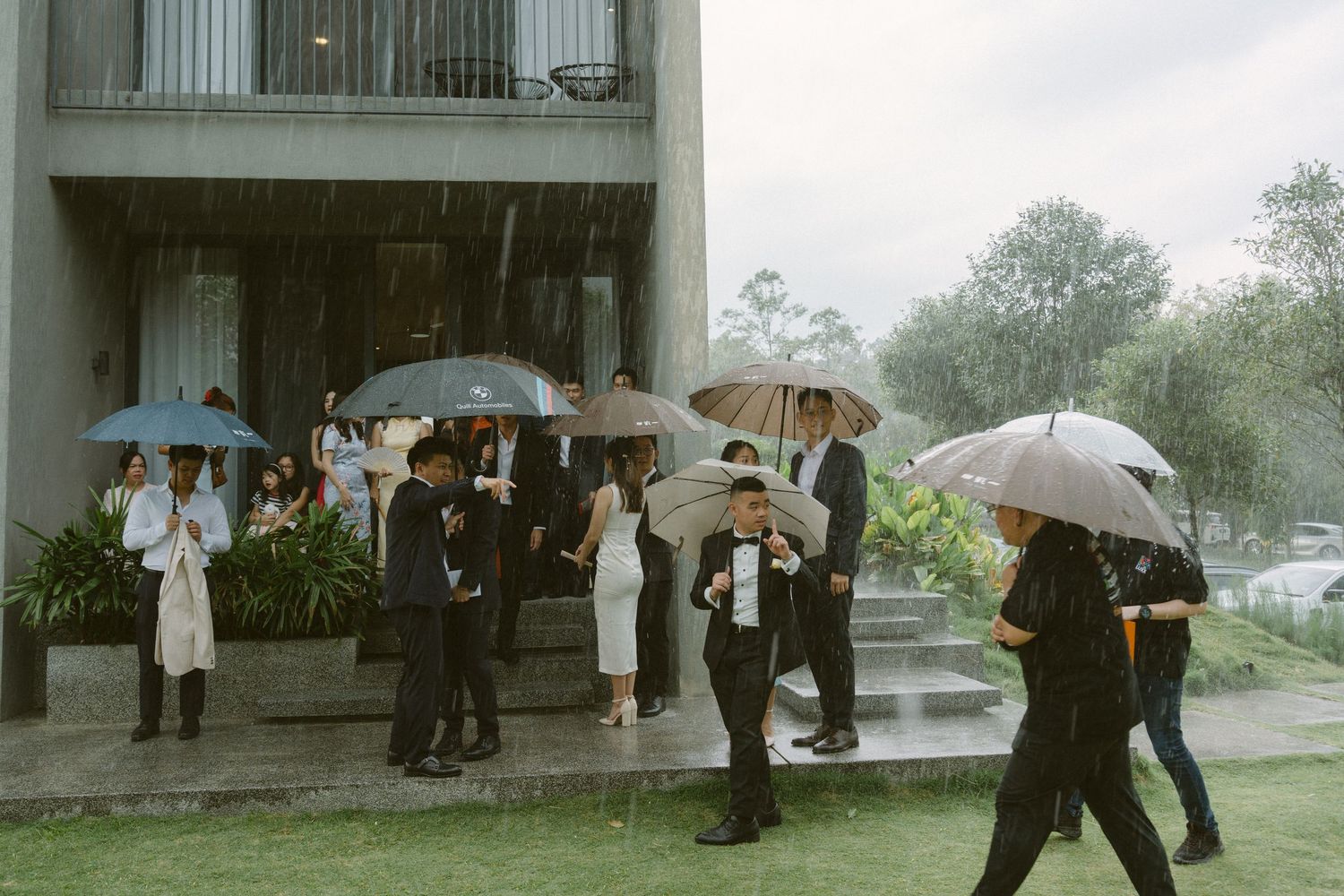 A group of people holding umbrellas stands outside a building in the rain during what appears to be a formal event.