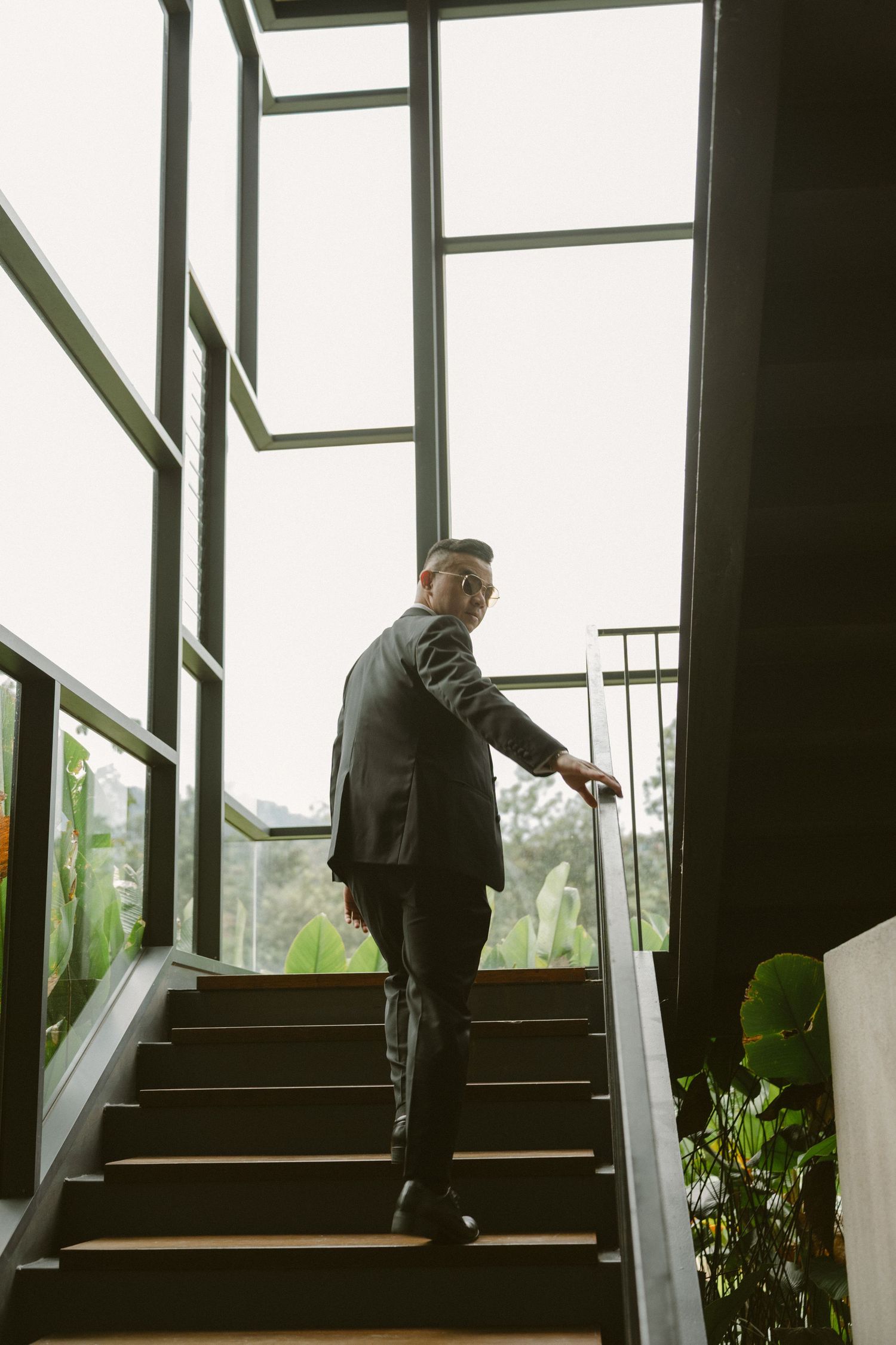 Person in dark attire ascending modern staircase with glass windows and natural lighting.