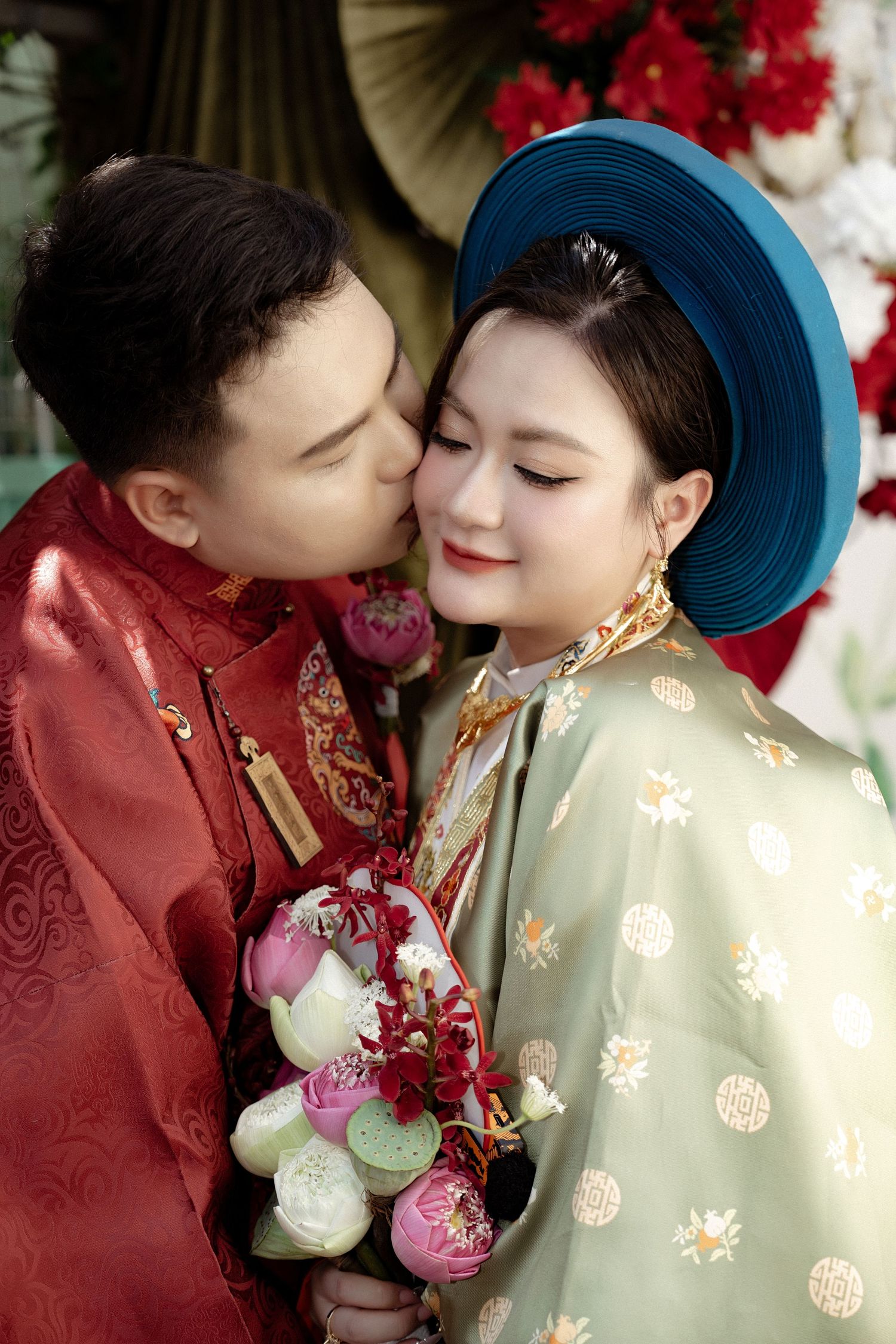 A romantic moment between a couple in traditional Vietnamese ao dai attire with blue hat and floral bouquet during engagement photos.