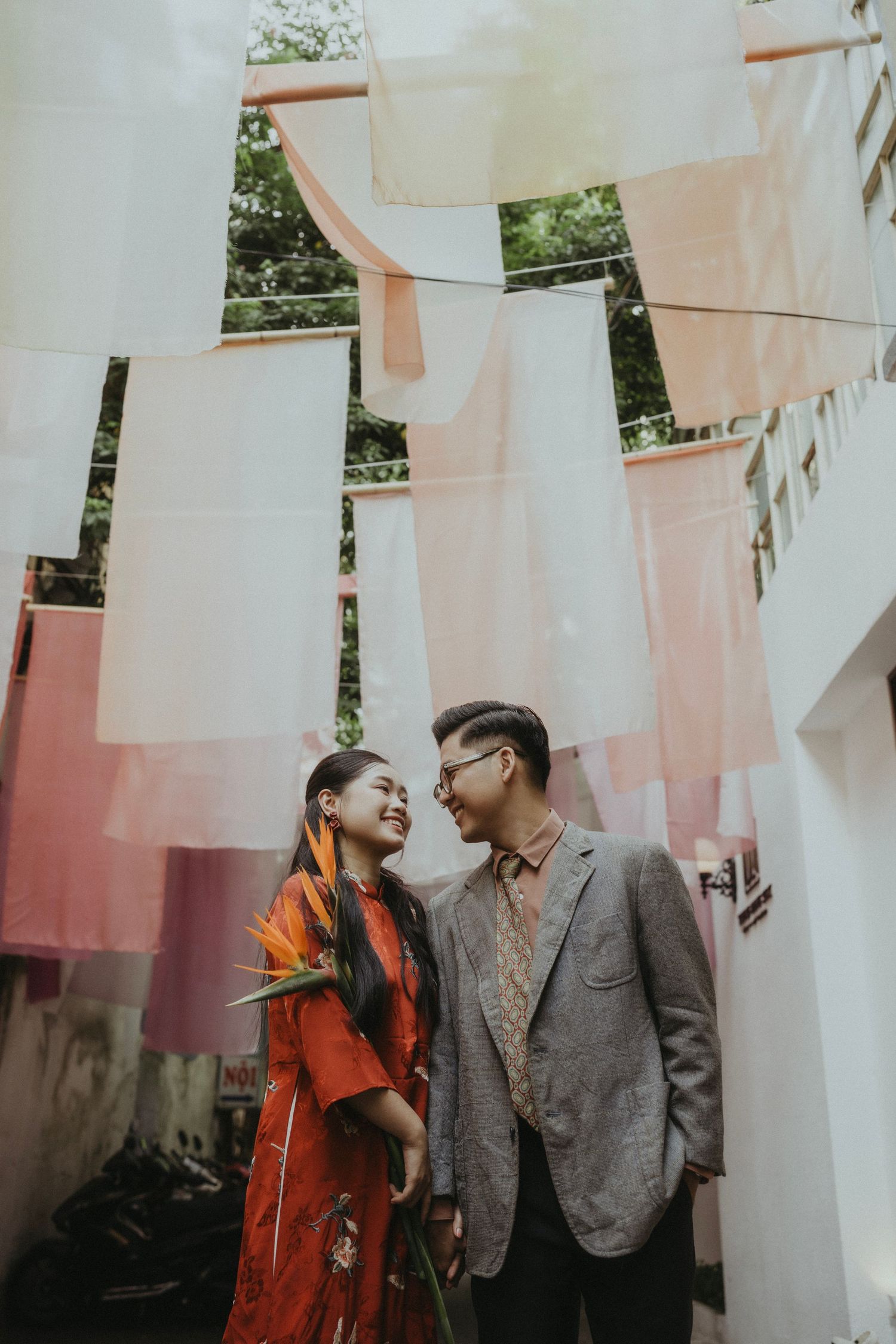 A couple shares a romantic moment under hanging laundry with sunlit white sheets creating a dreamy atmosphere.