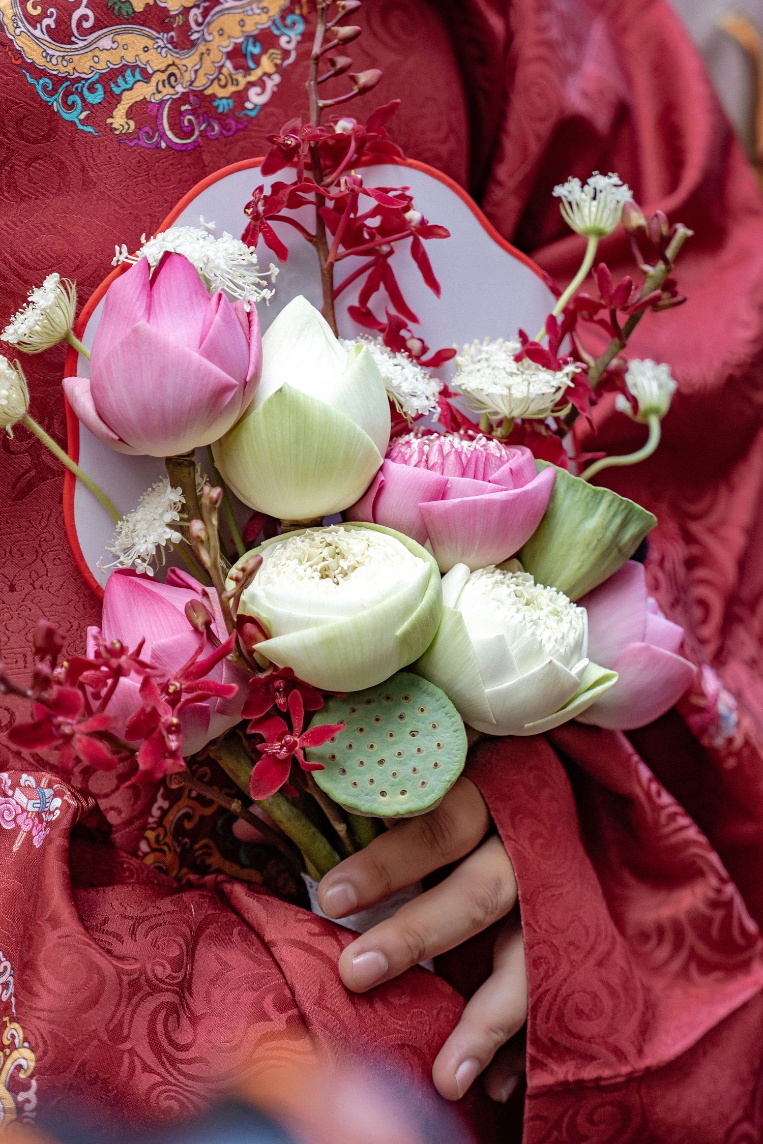A delicate bouquet of white and pink lotus blossoms against a red silk brocade fabric with embroidered designs.