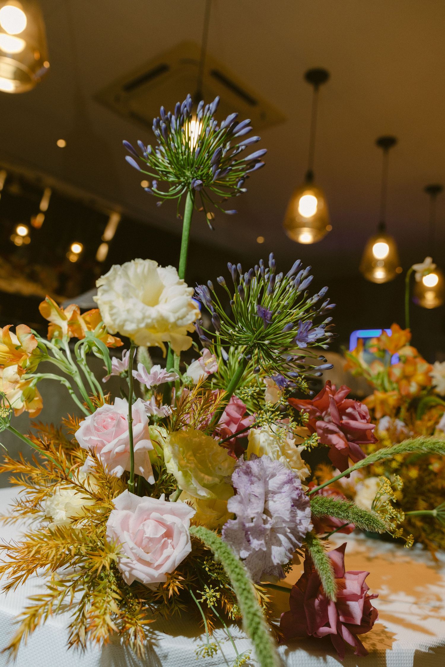 Beautiful centerpiece arrangement of pink roses, purple blooms, and golden foliage for an elegant indoor table setting.
