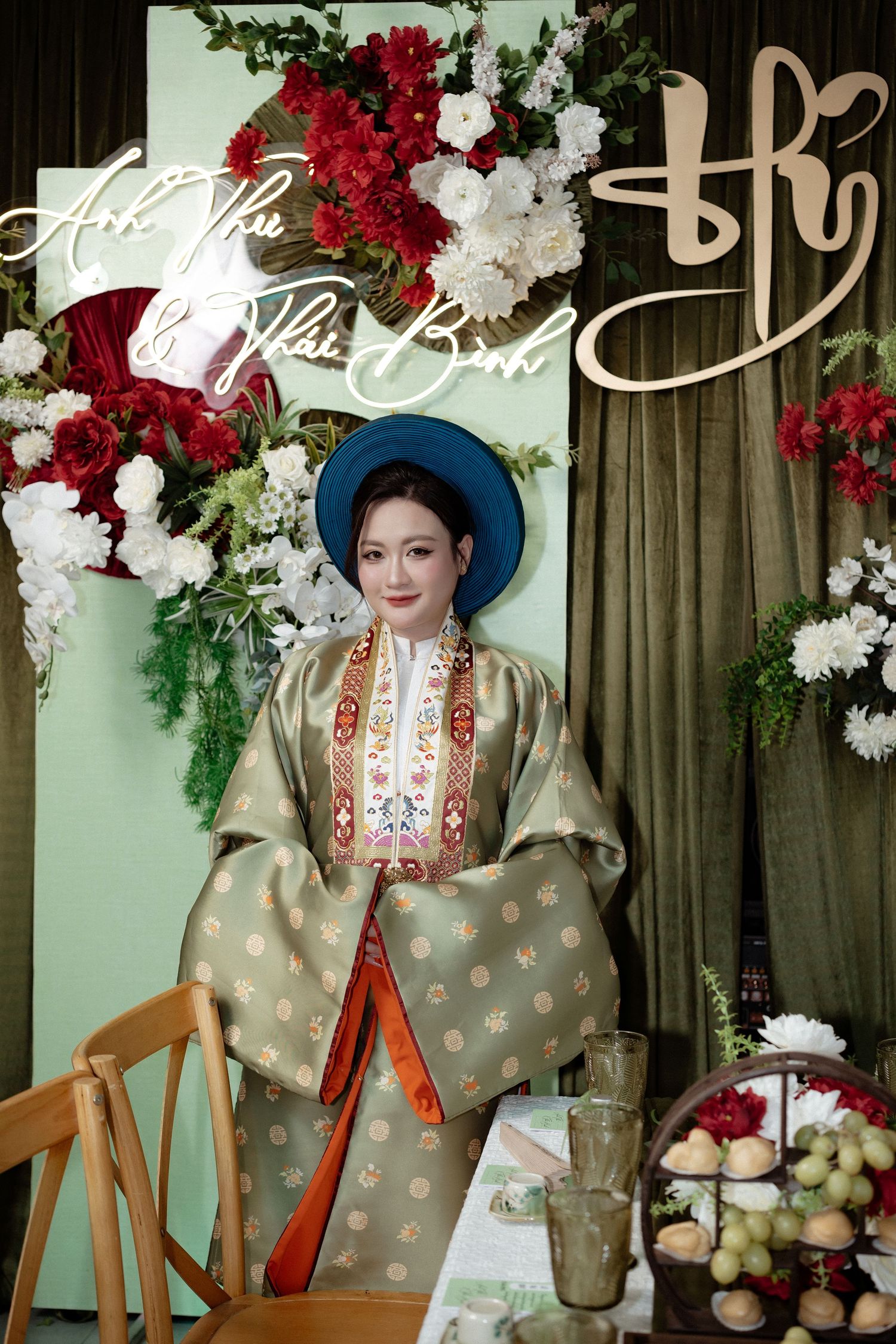 Elegant traditional Vietnamese wedding decor with red and white floral arrangements and greenery against a sage backdrop.