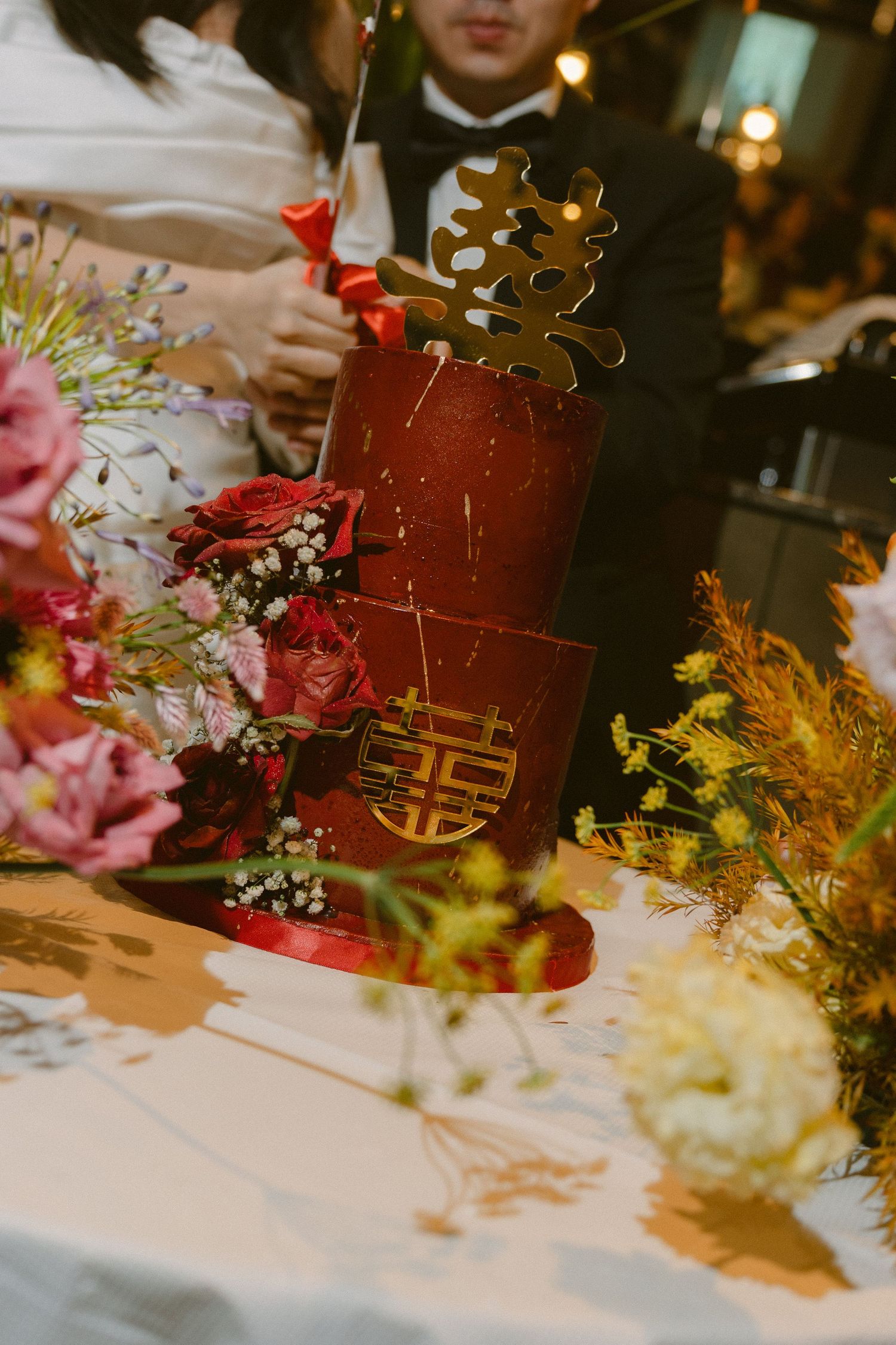 Elegant wedding table setting with red and pink floral centerpieces arranged along white linen tablecloth.
