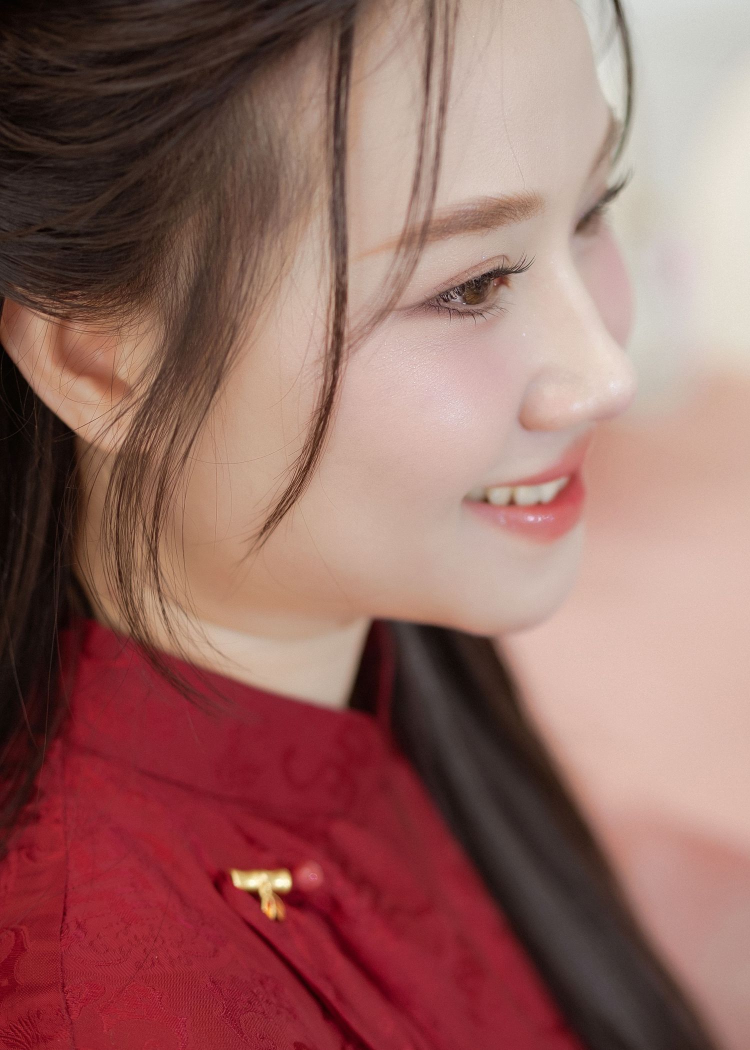Side profile view of a smiling person wearing a red traditional Chinese style high-neck top with a small gold accent pin.