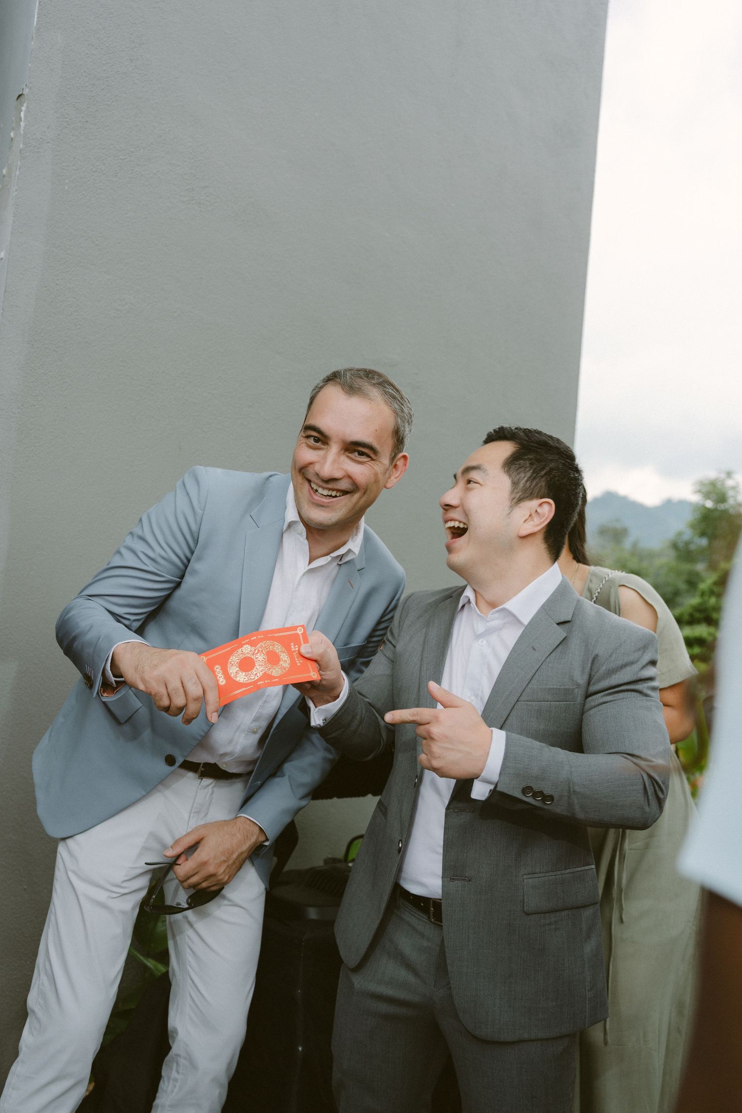 Two men in gray suits share a lighthearted moment while laughing and gesturing during a formal event.