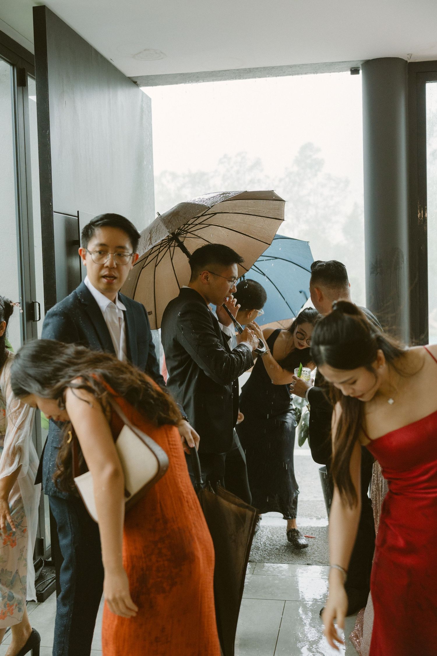 A formal event gathering on a balcony where guests hold umbrellas while wearing elegant dresses and suits.