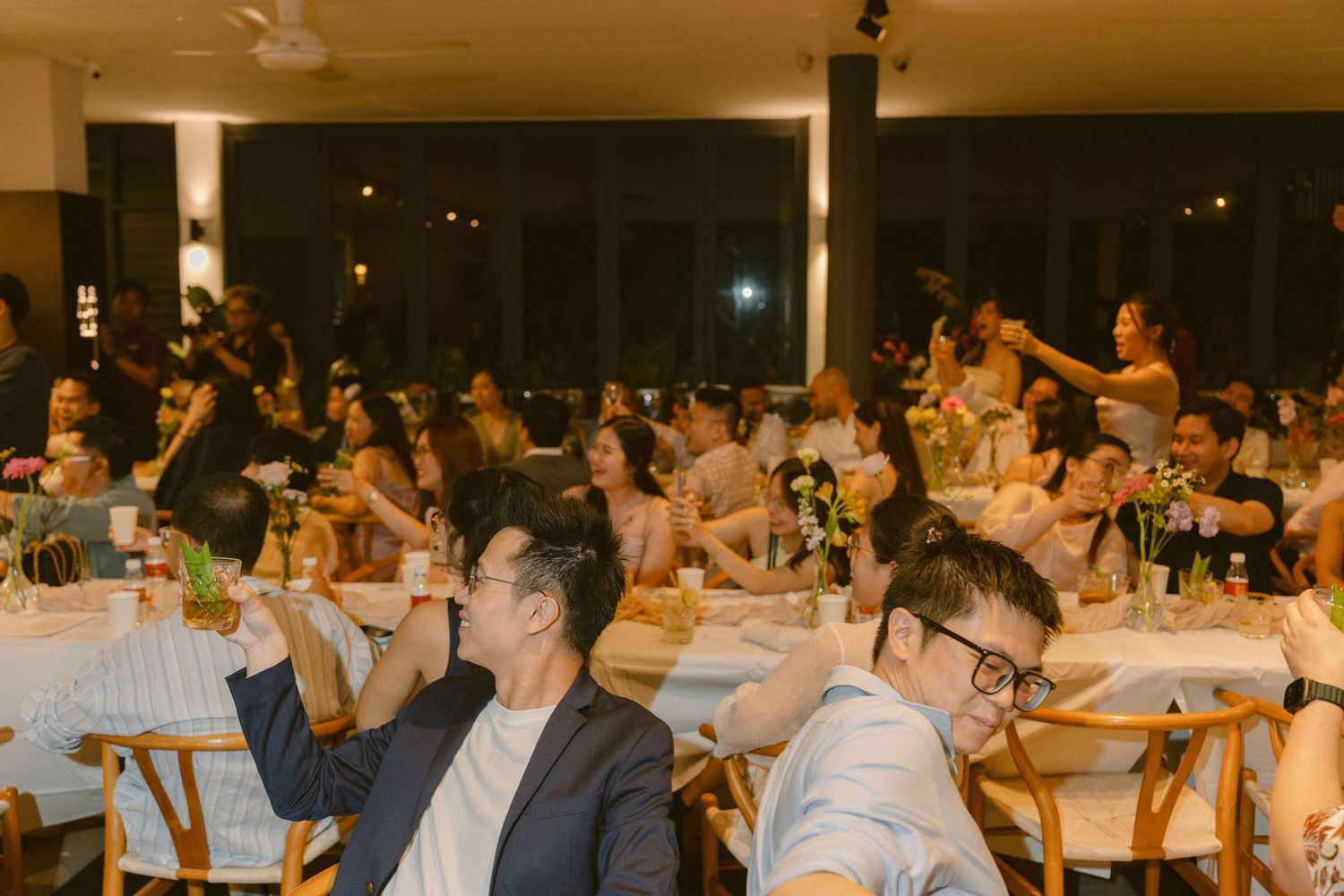 People gather around tables in a dimly lit event space during an evening gathering.