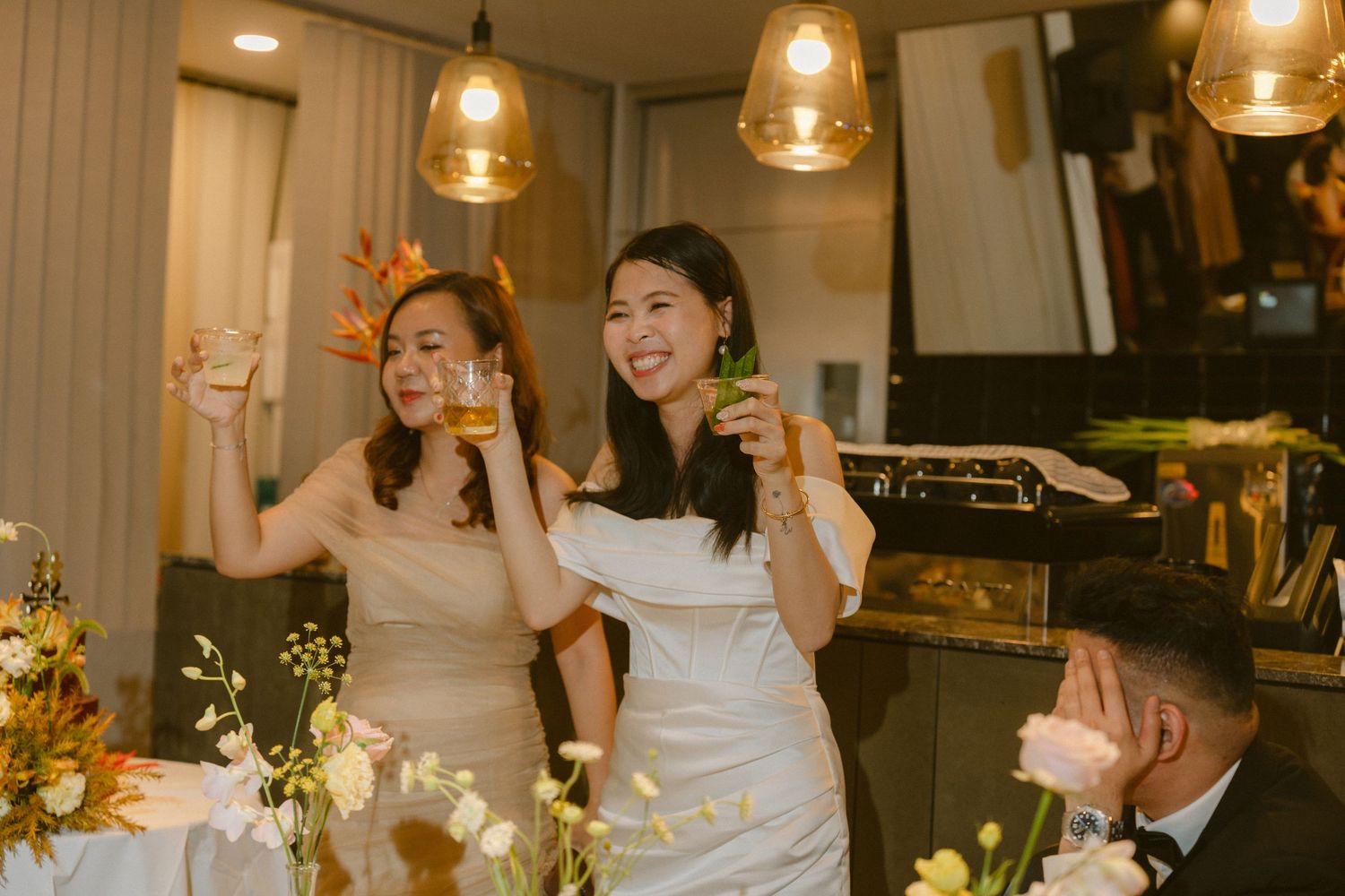 People celebrate with raised drinks at an elegant indoor party with warm lighting and table decorations.