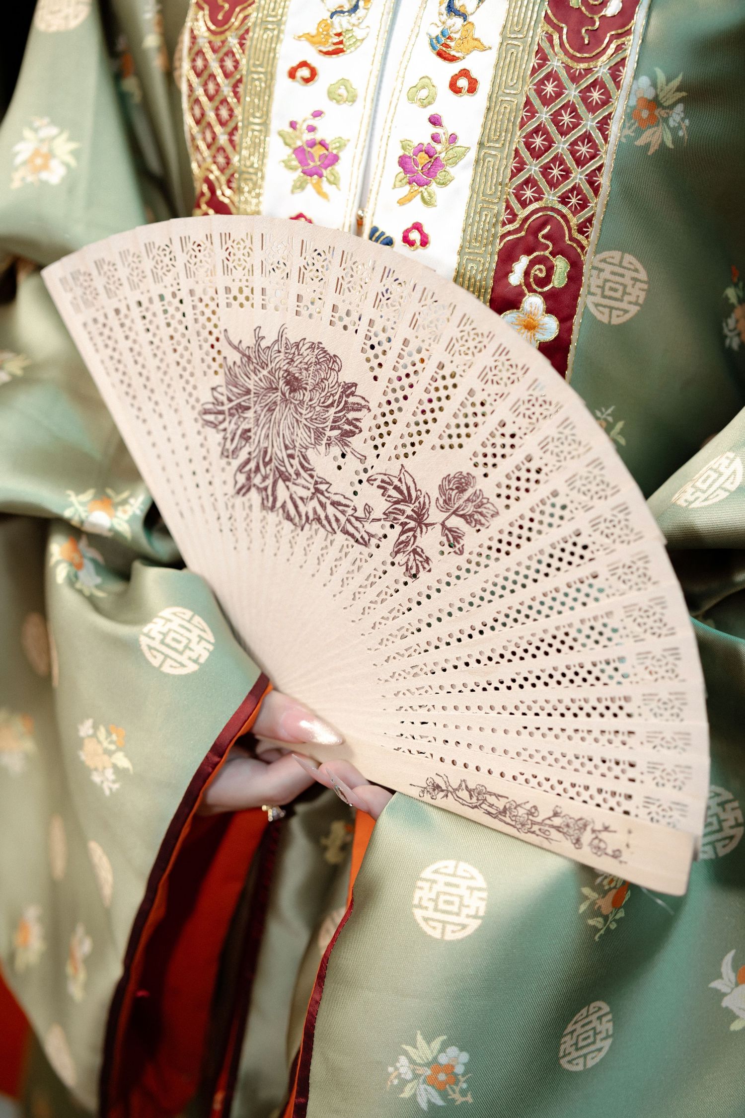 A delicate white lace fan held against a traditional mint green kimono with floral patterns and red trim.