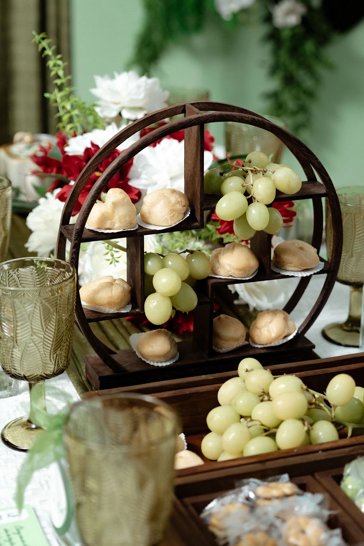Elegant wooden circular display stand with macarons and green grapes on a decorated table setting with glassware.
